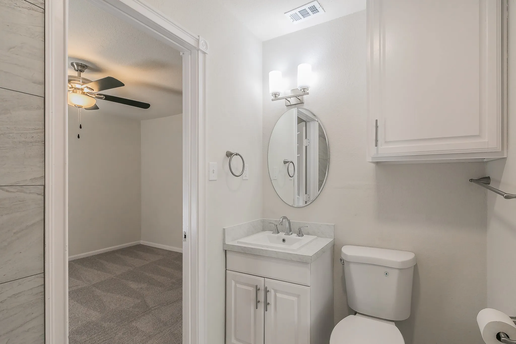 Bathroom featuring a single vanity with under-sink cabinetry, an oval mirror, wall-mounted light fixture, and built-in wall cabinet