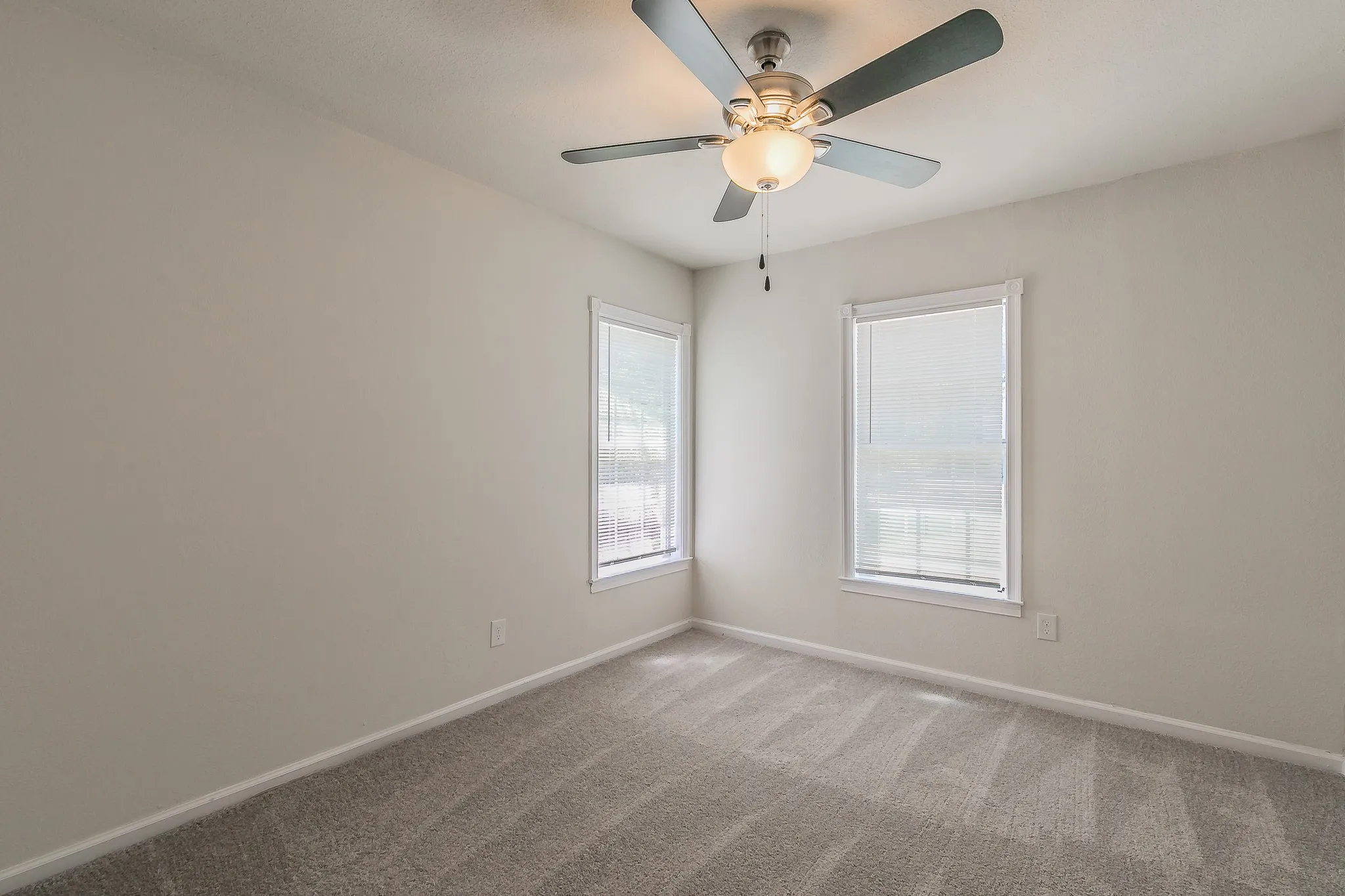 Neutral-toned walls, ceiling fan with integrated lighting, two windows with blinds, and light-colored carpet flooring