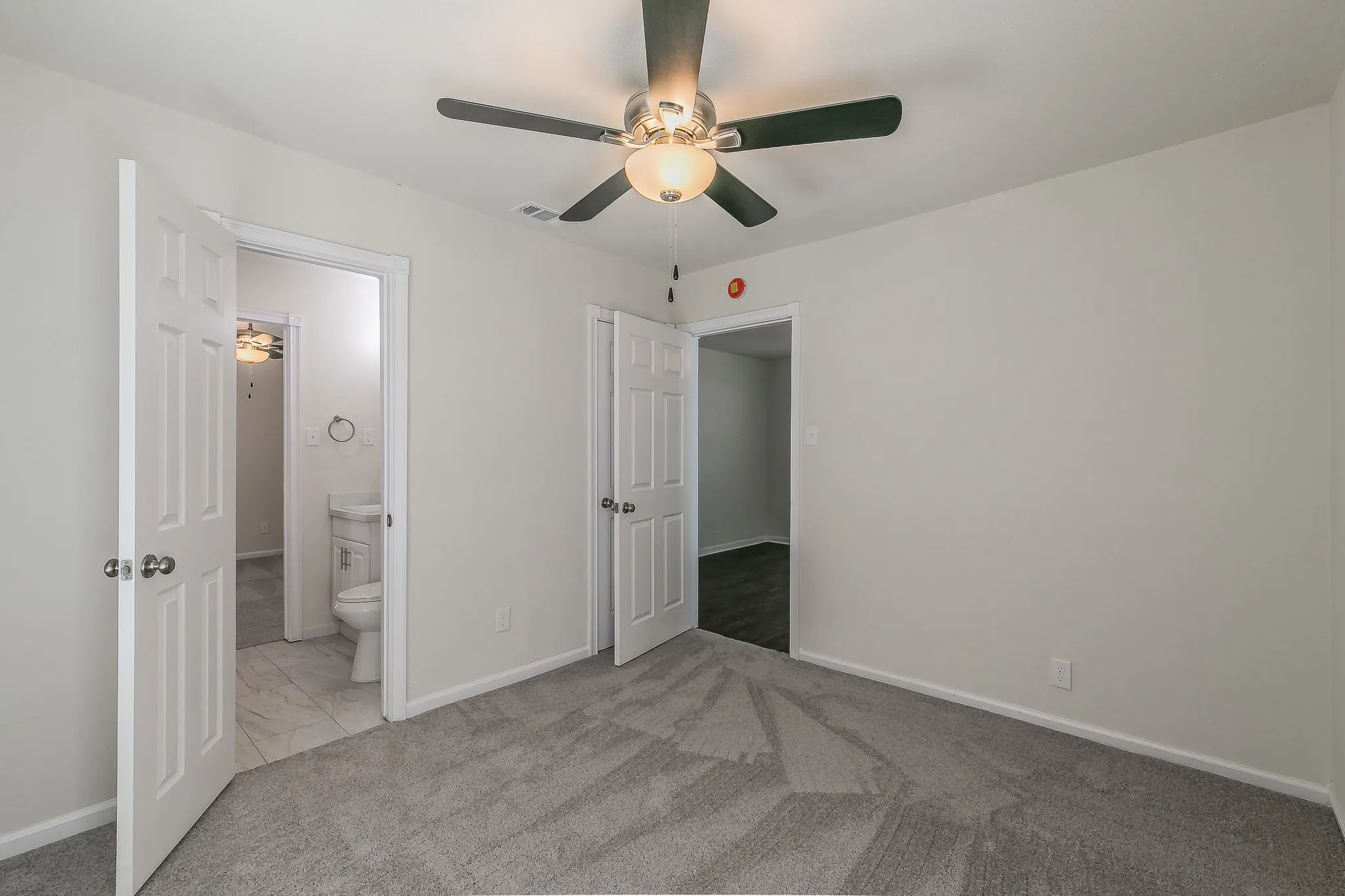 Plush grey carpeting, white interior doors, and a ceiling fan with integrated lighting