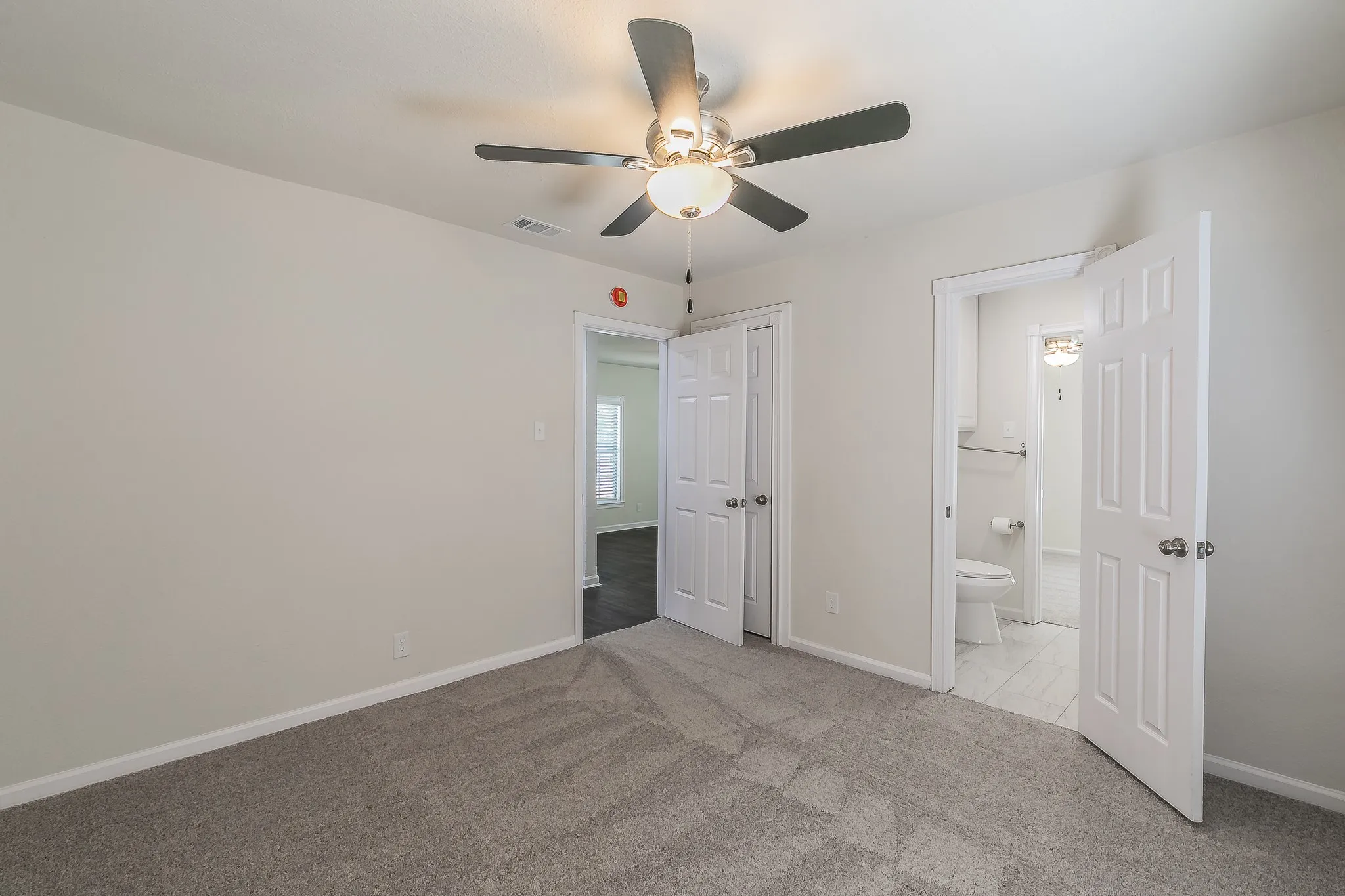 Neutral wall paint, ceiling fan with integrated lighting, textured gray carpeting, and white paneled doors