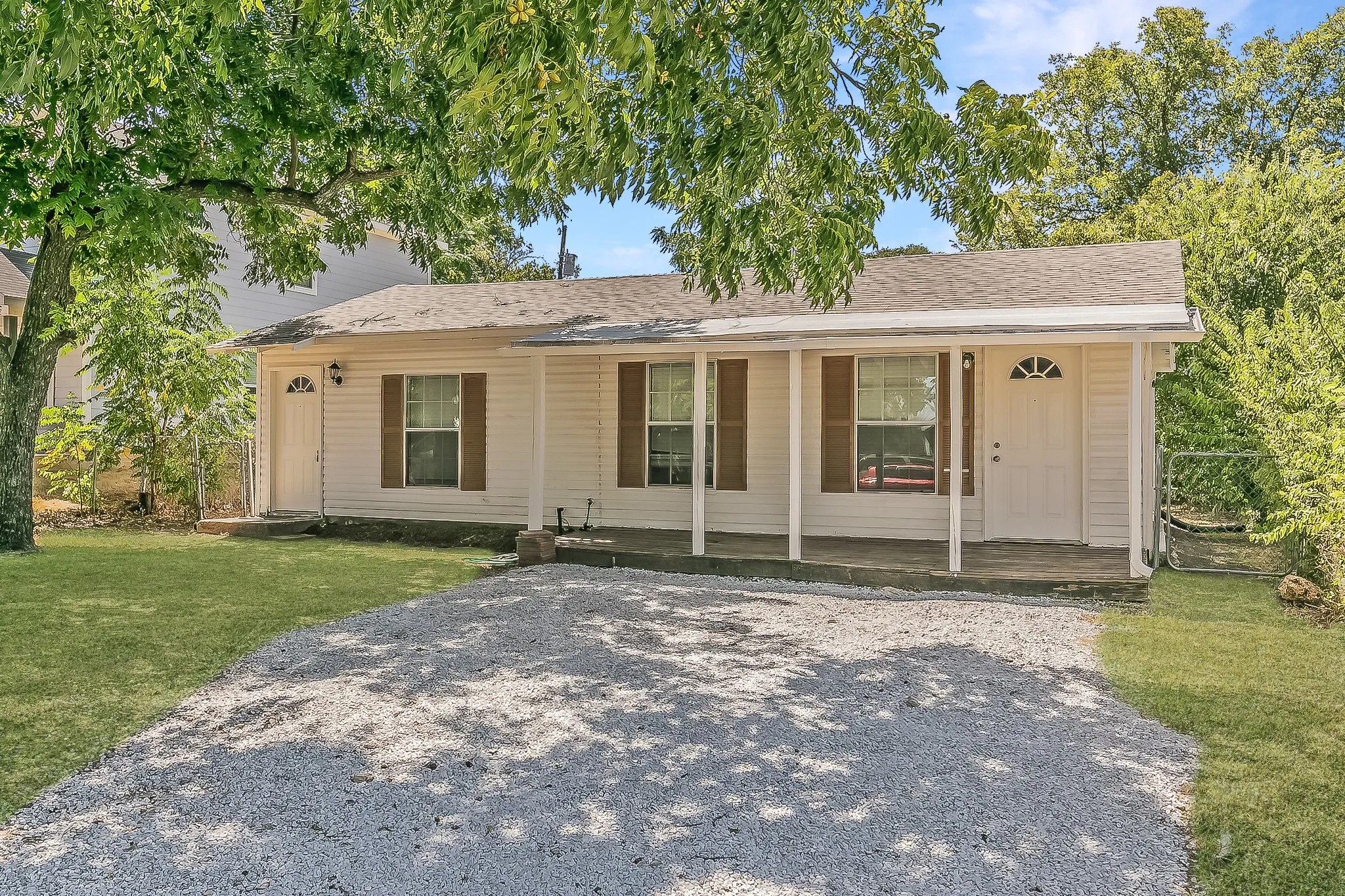 Single-story residence featuring a covered front porch with white pillars, light-colored siding, and a gravel driveway