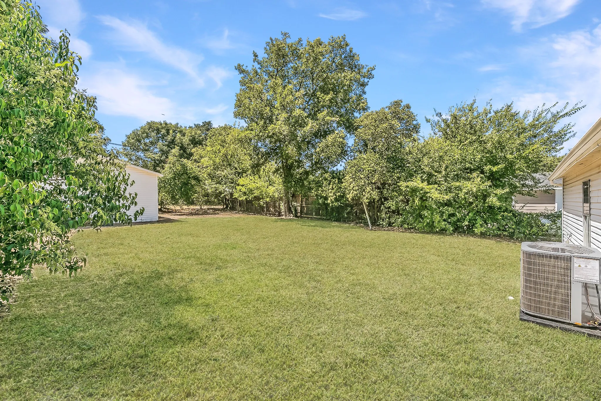 Expansive lawn with surrounding mature trees and a detached structure