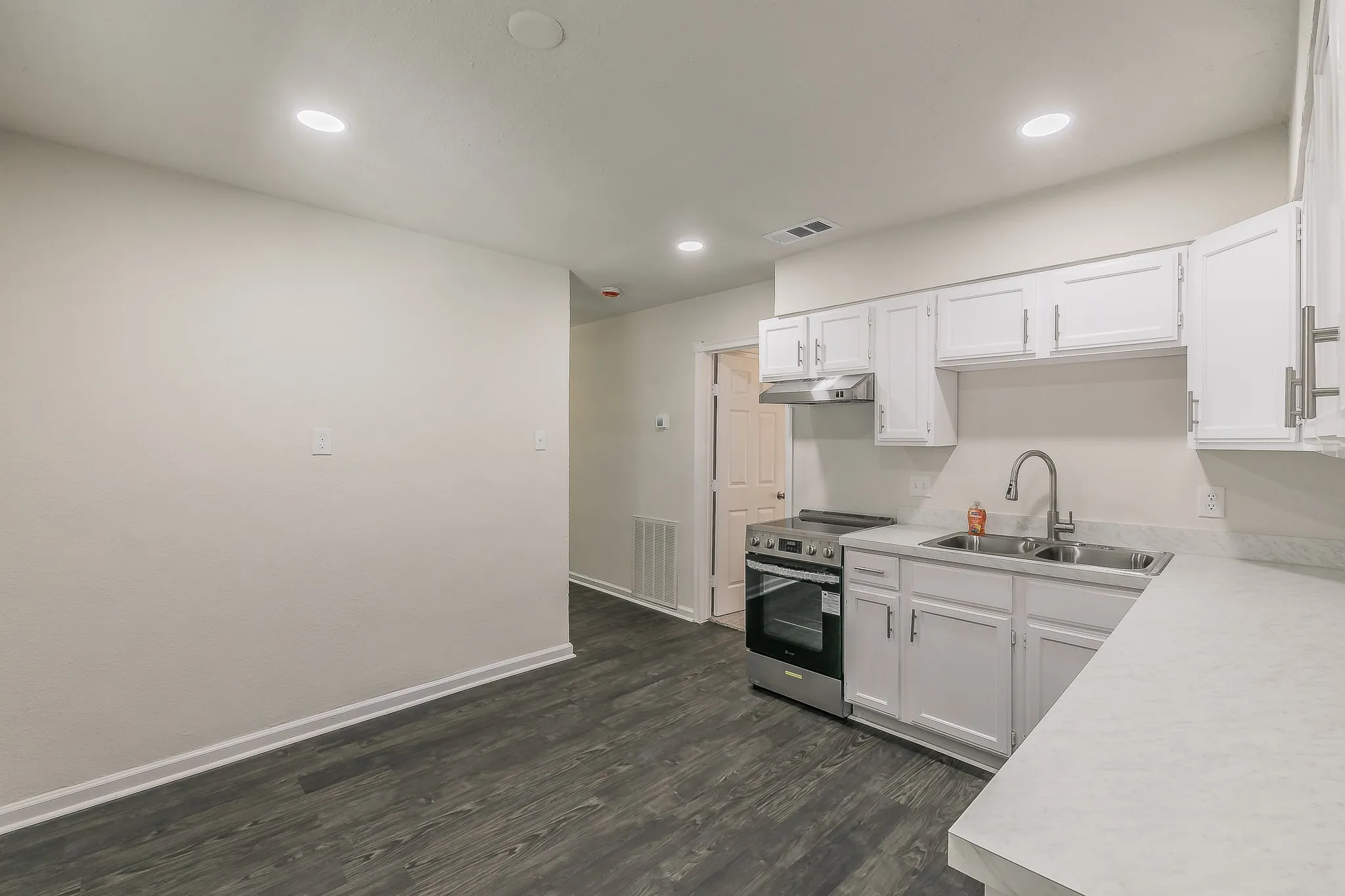 Kitchen featuring white cabinetry, stainless steel range, double basin sink, light-toned countertops, and wood-finish flooring