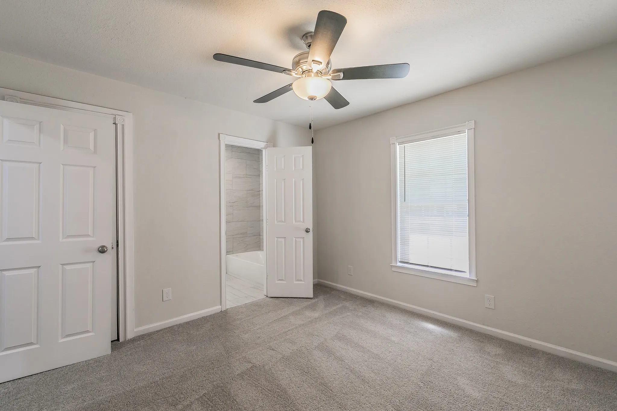 Neutral tone walls with gray carpet flooring, ceiling fan with integrated lighting, and a window with blinds