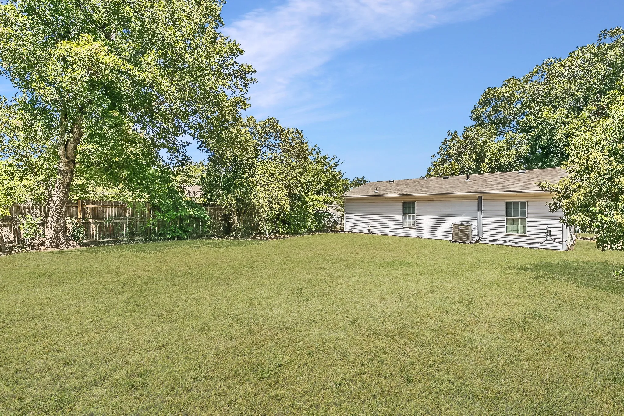 Expansive lawn bordered by a wood fence, mature trees, and a siding exterior