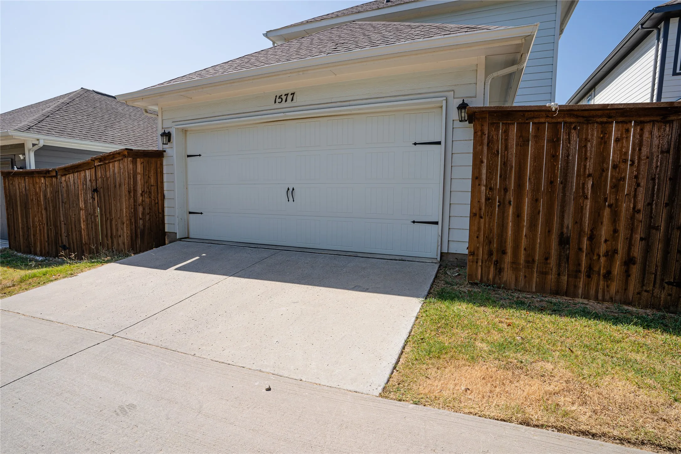 Attached garage with overhead door, concrete driveway, and wood fencing