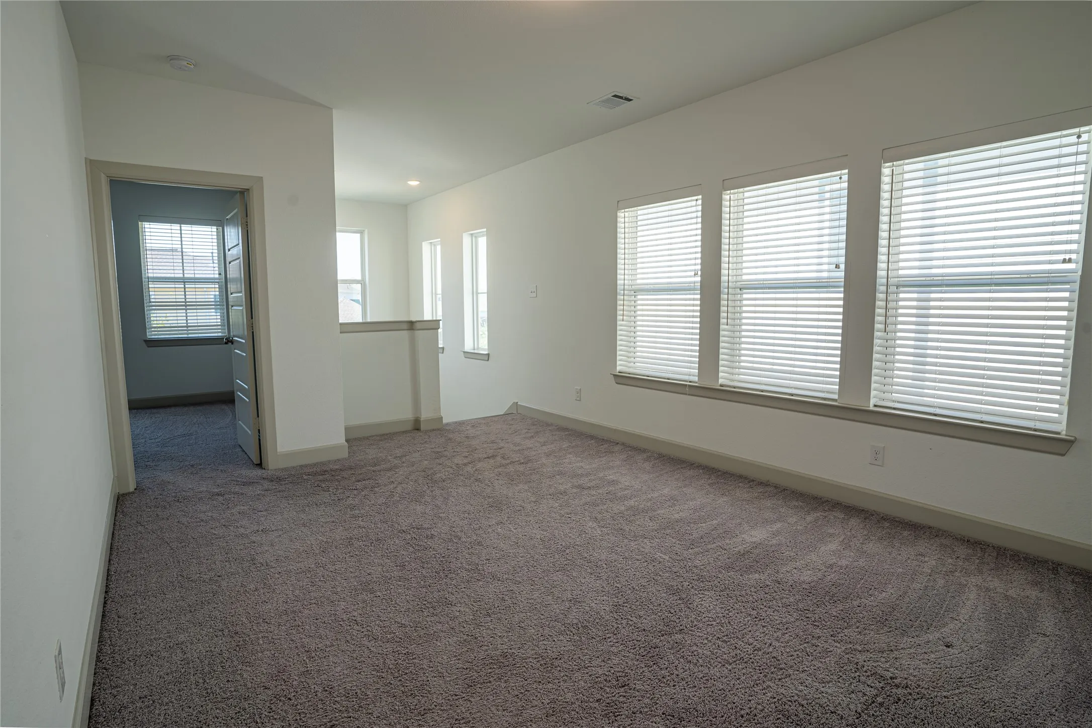 Carpeted interior with multiple large windows, white walls, and a partial low wall
