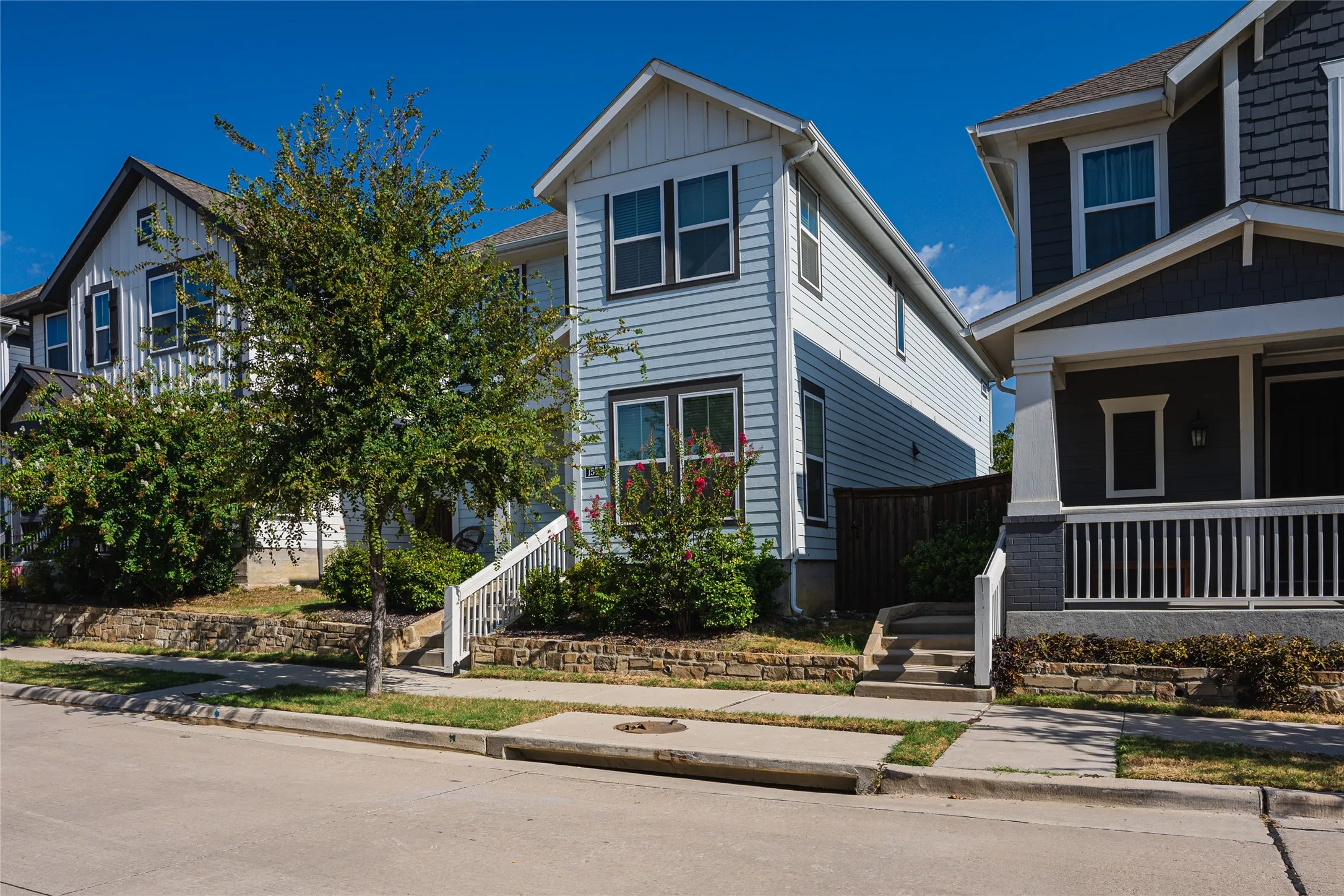 Two-story residence with light blue siding, white trim, dark window frames, and a gable roofline