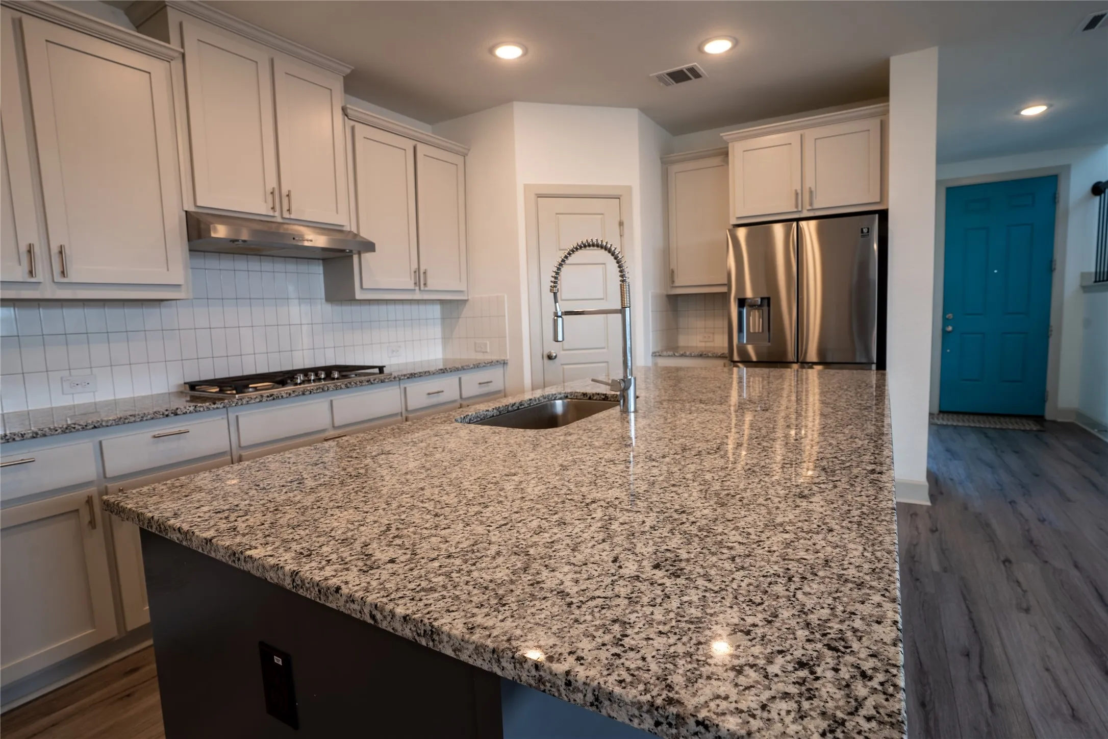 Kitchen featuring granite countertops, stainless steel appliances, a white tile backsplash, and light-colored cabinetry