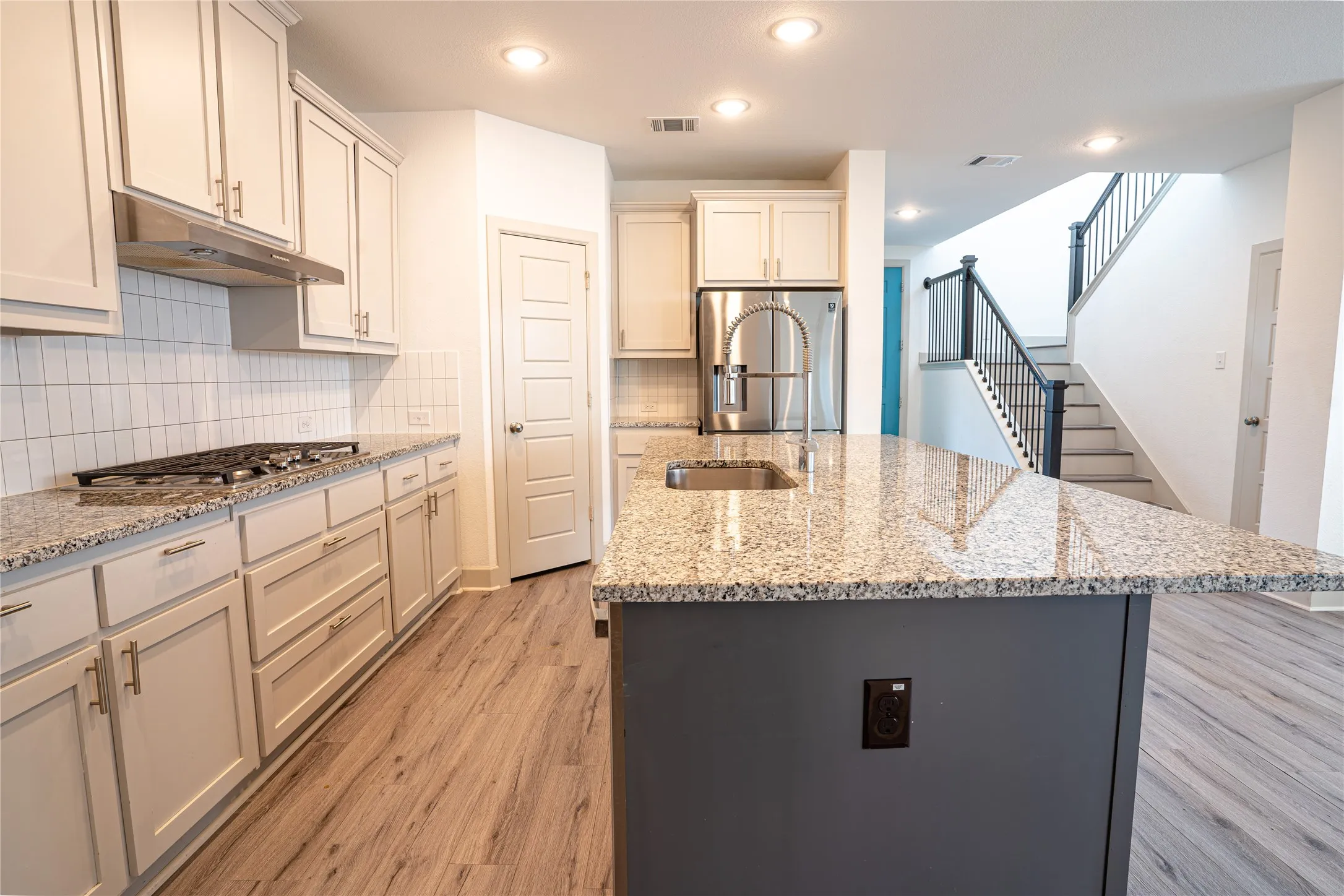 Kitchen featuring granite countertops, wood-finish flooring, white cabinetry, a stainless steel gas range, and a kitchen island with an integrated sink