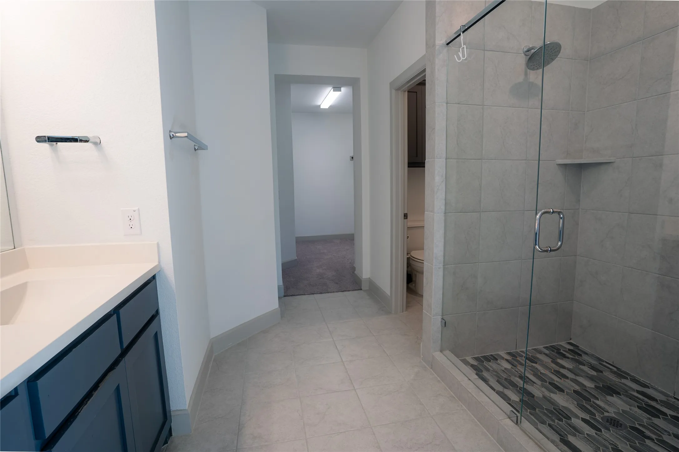 Spacious bathroom featuring a glass-enclosed shower with a tiled surround, a built-in shower shelf, and a mosaic tile shower floor