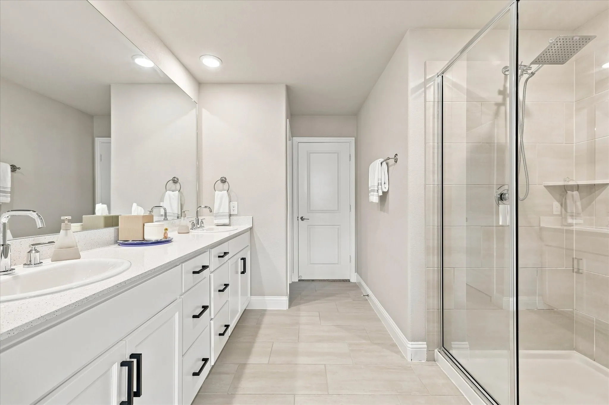 Dual vanity with under-mount sinks, expansive wall-mounted mirror, frameless glass shower enclosure, and tiled shower surround with built-in shelf