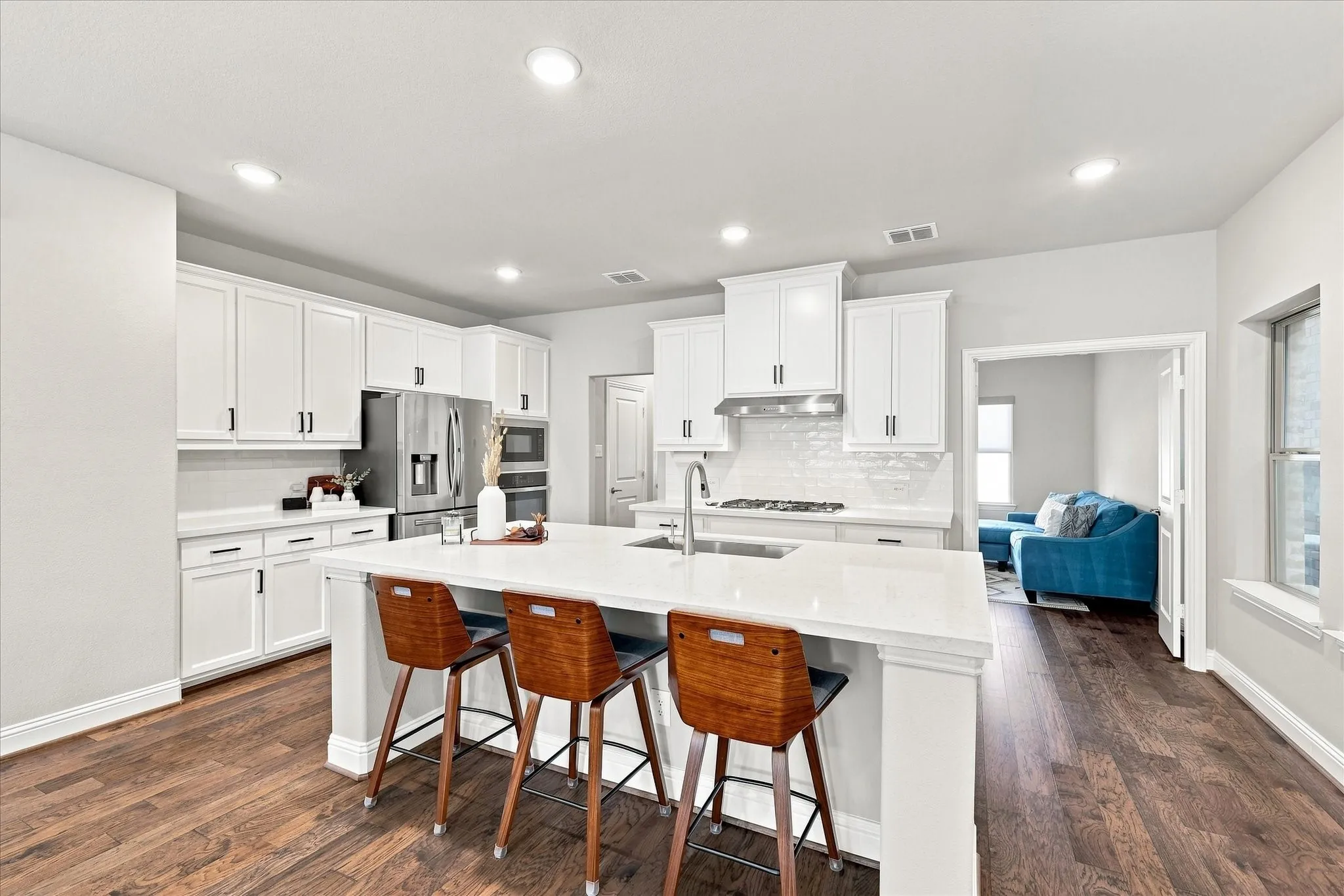 Kitchen featuring a large central island, white cabinetry, integrated stainless-steel appliances, a tile backsplash, and wood-finish flooring