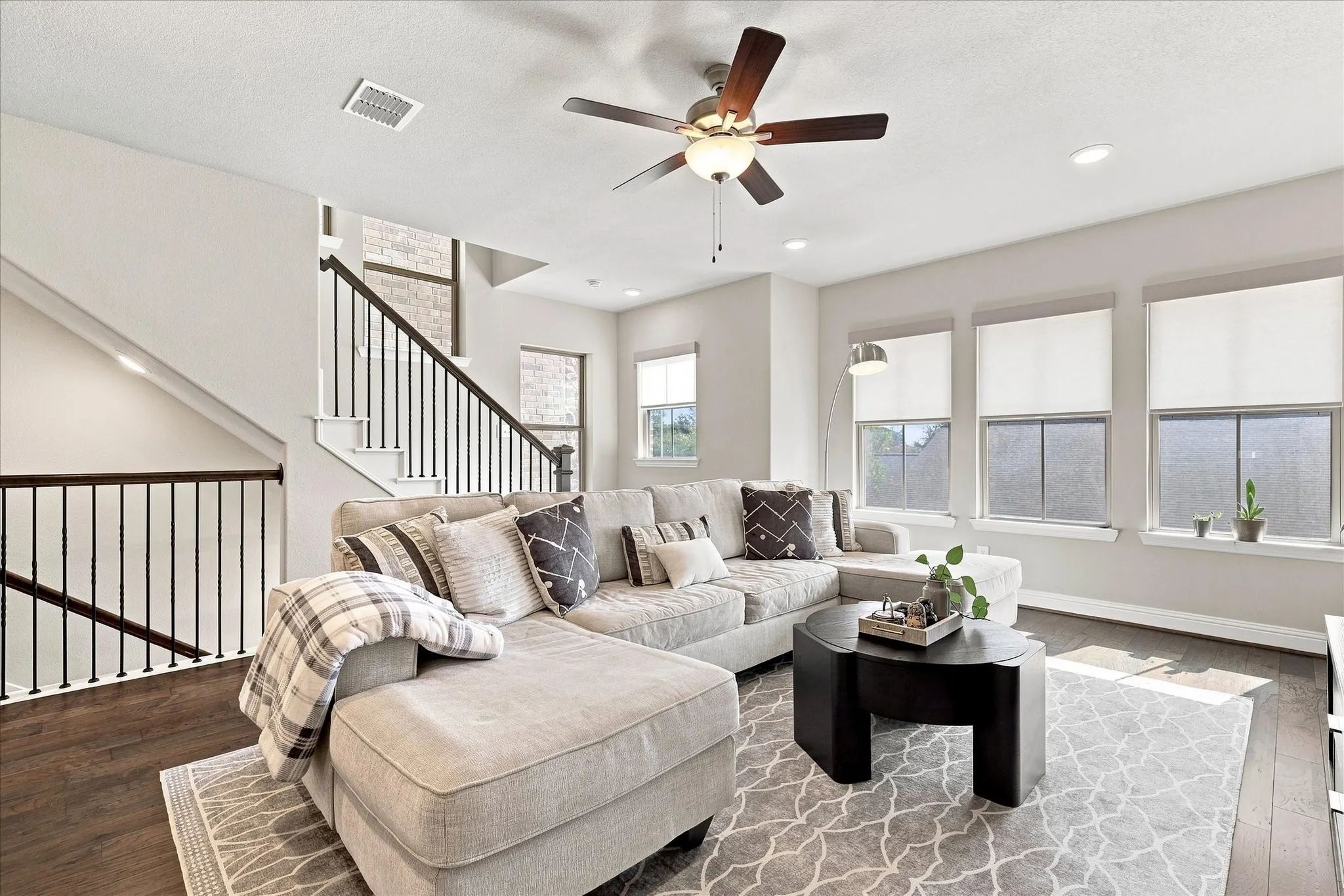 Open-concept living space featuring wood-finish flooring, a contemporary ceiling fan, recessed lighting, and multiple windows with roller shades