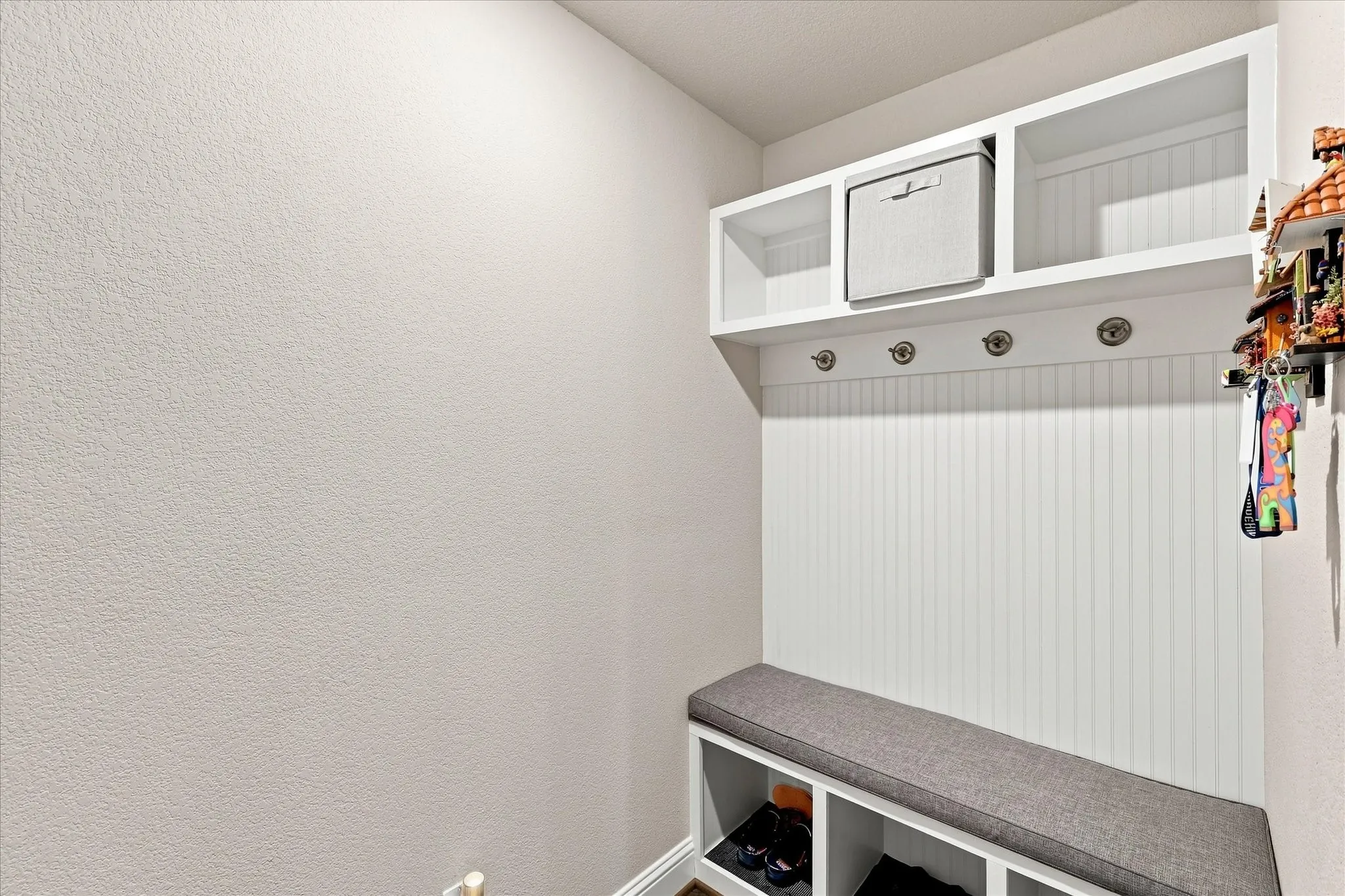 Built-in bench with storage cubbies, beadboard paneling, upper shelving, and wall-mounted hooks