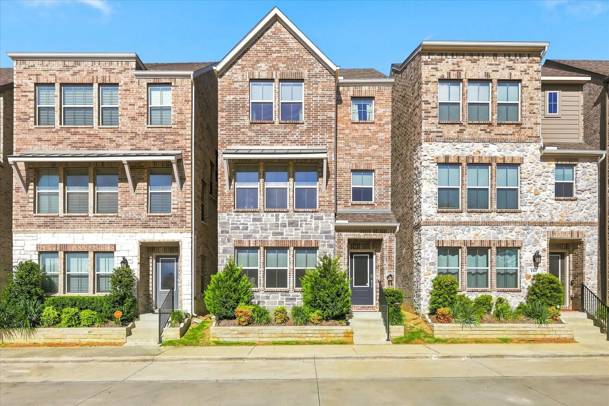 Brick and stone exterior with multiple windows, featuring a prominent gable roofline, landscaped entryways, and exterior lighting fixtures
