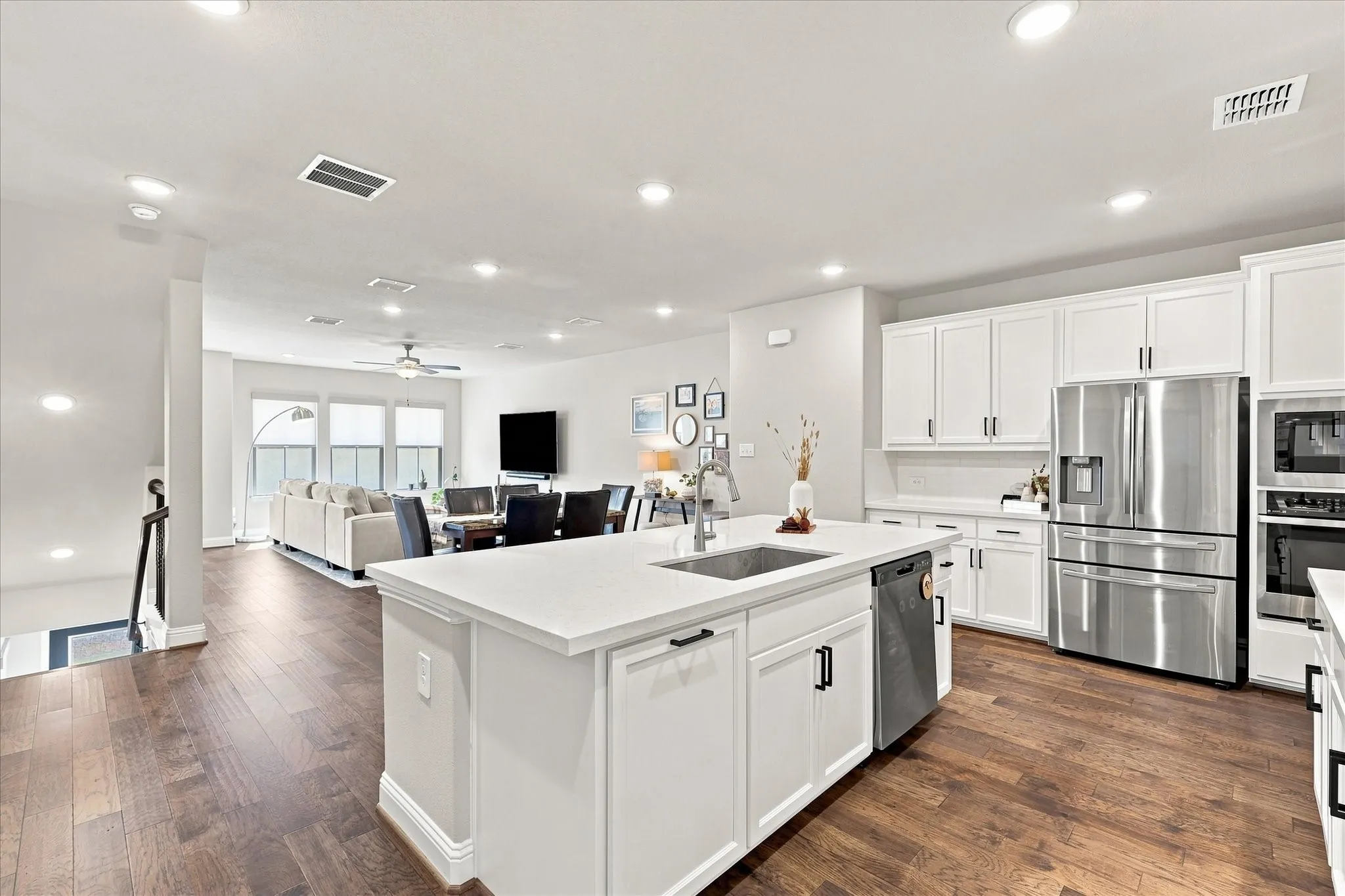 Open-concept kitchen with a large island, white cabinetry, integrated stainless steel appliances, and wood-finish flooring