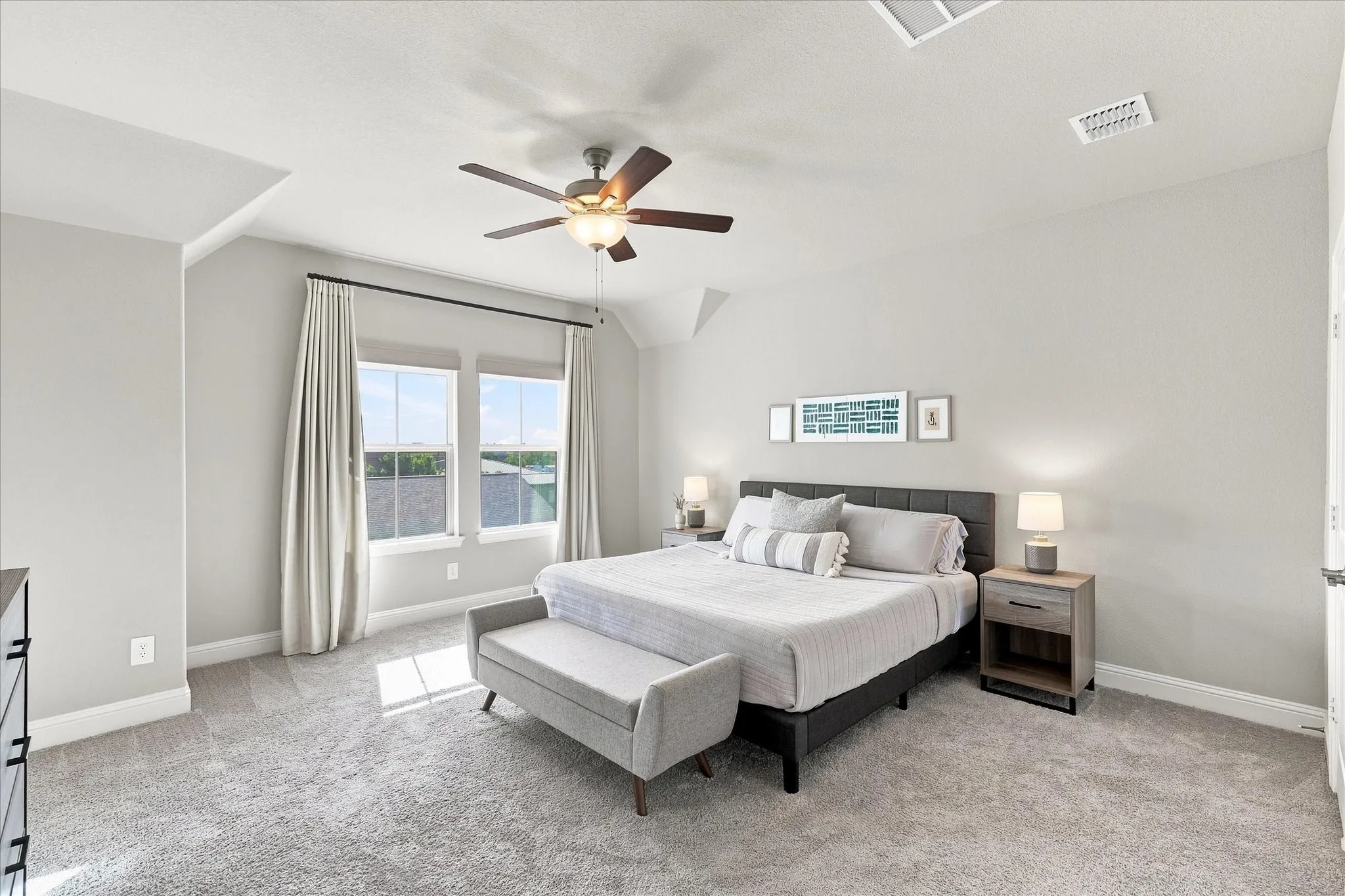 Plush carpet flooring, light gray wall finishes, dual windows with black curtain rods, and a ceiling fan with integrated lighting