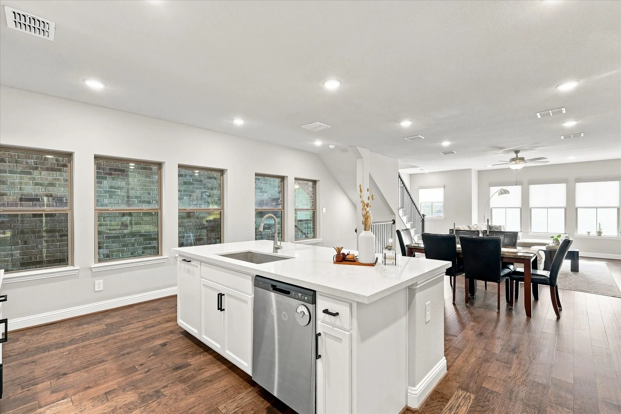 Kitchen island with integrated sink and stainless steel dishwasher, white shaker cabinetry, light-toned countertop, and wood-finish flooring