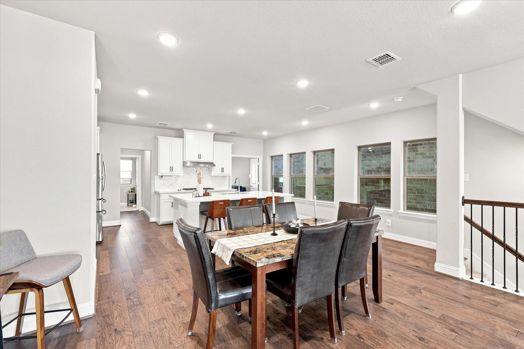 Wood-finish flooring throughout, recessed lighting, white walls, and a staircase with black metal balusters