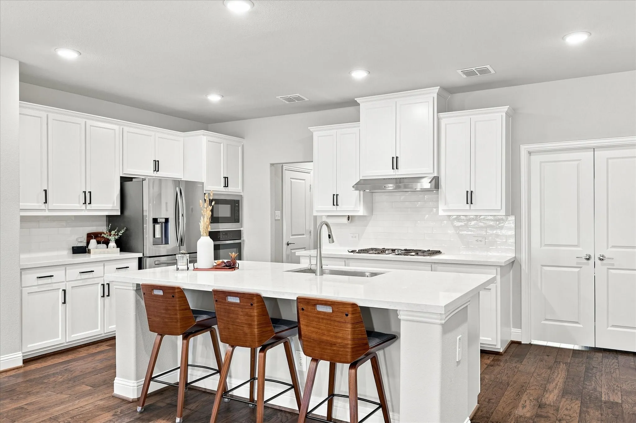 White shaker cabinetry, stainless steel appliances, central island with seating, white countertops, and wood-finish flooring