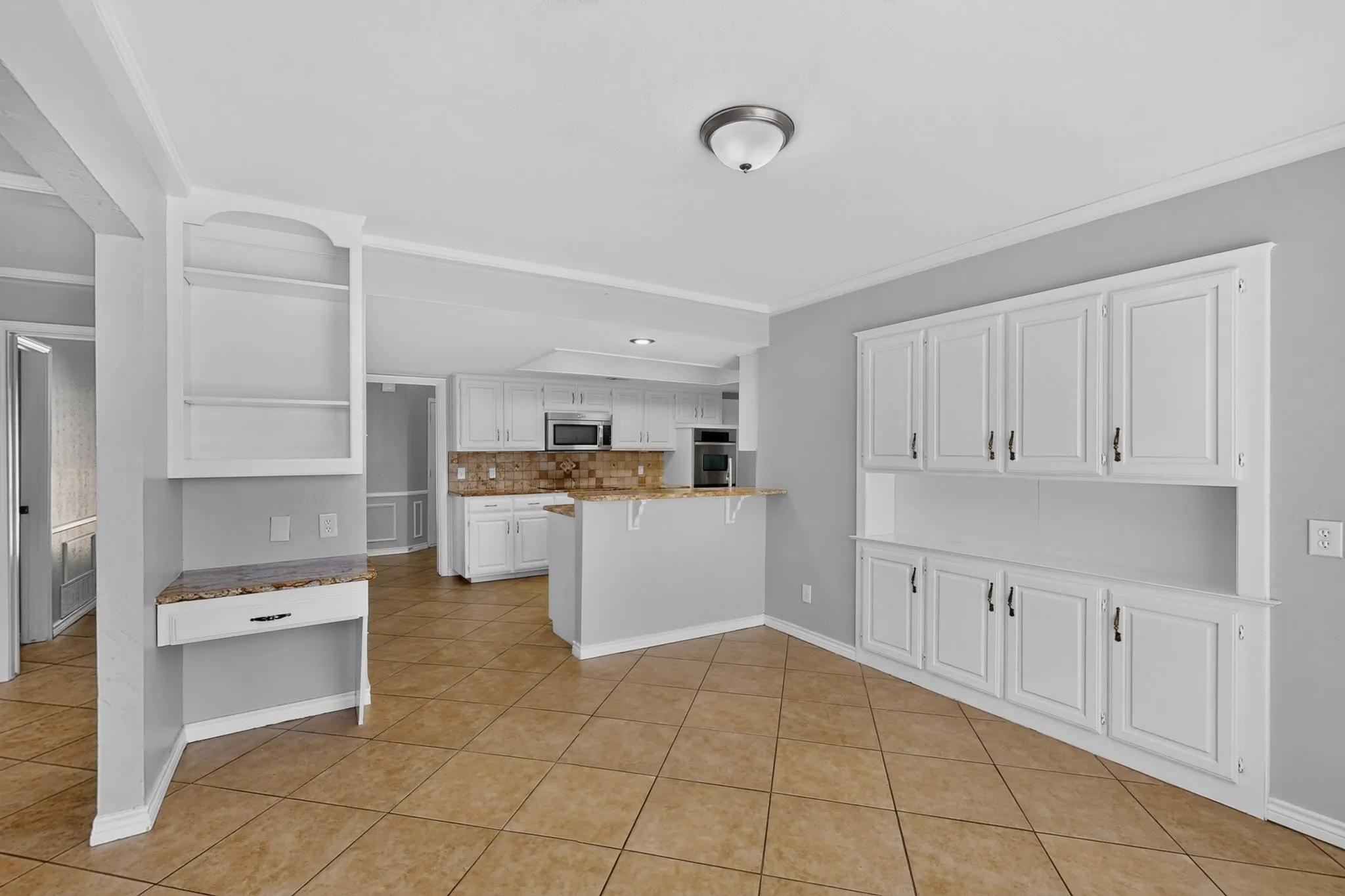 Built-in cabinetry with white finishes, tile flooring, and a kitchen featuring white cabinetry, integrated microwave, and a counter-height bar