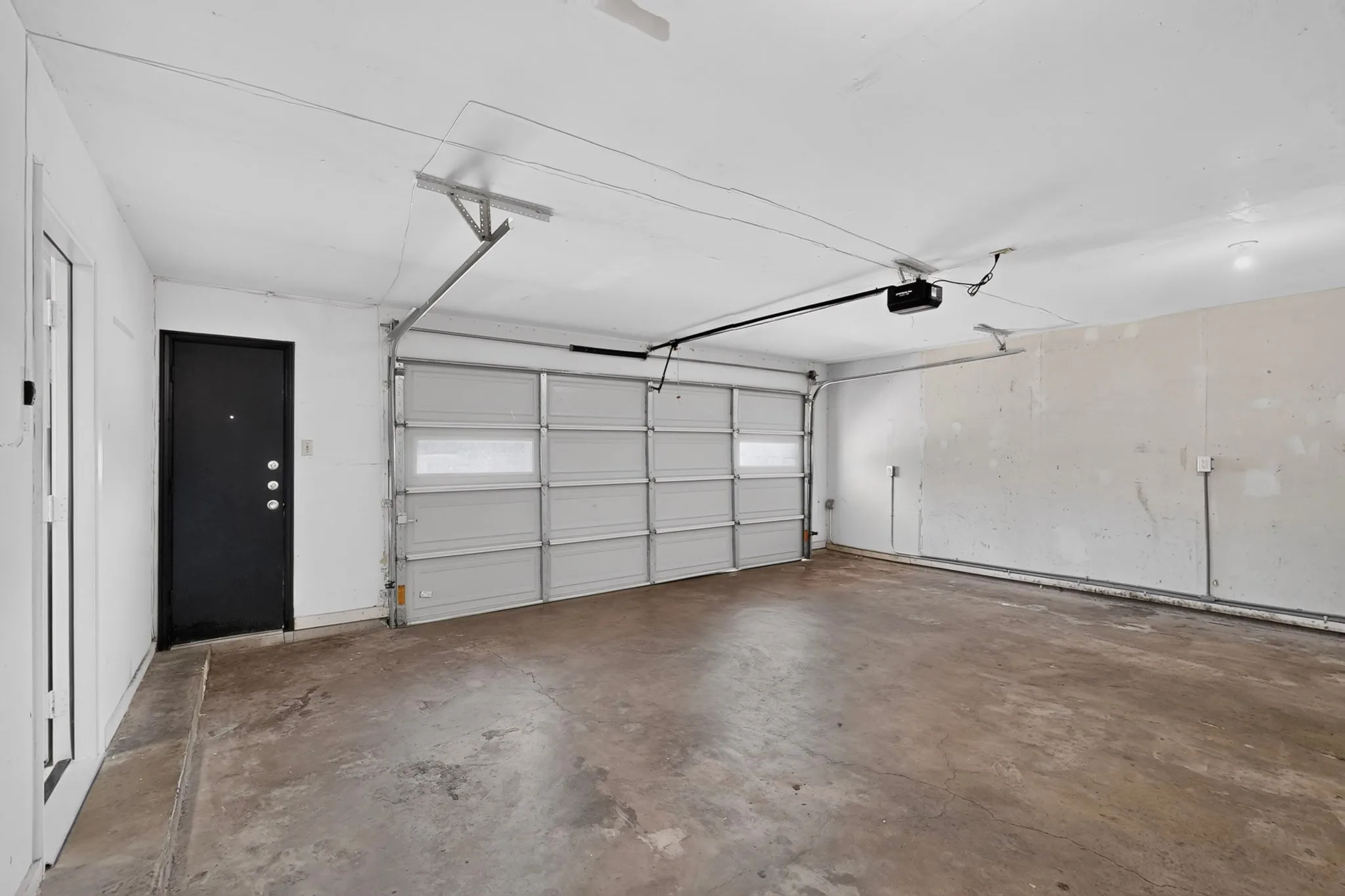 Attached garage with a concrete floor, an overhead garage door, and a black entry door