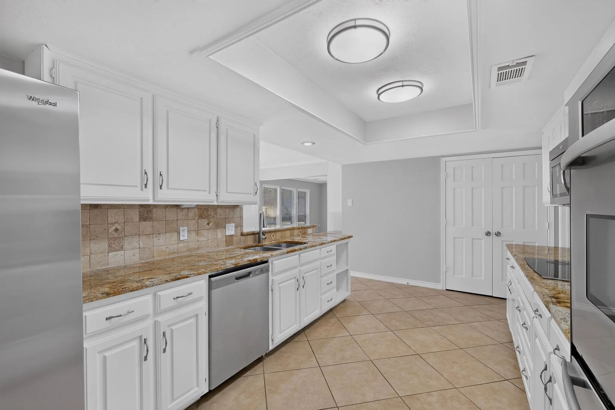 White cabinetry, stainless steel appliances, tile flooring, stone countertops, and a tile backsplash