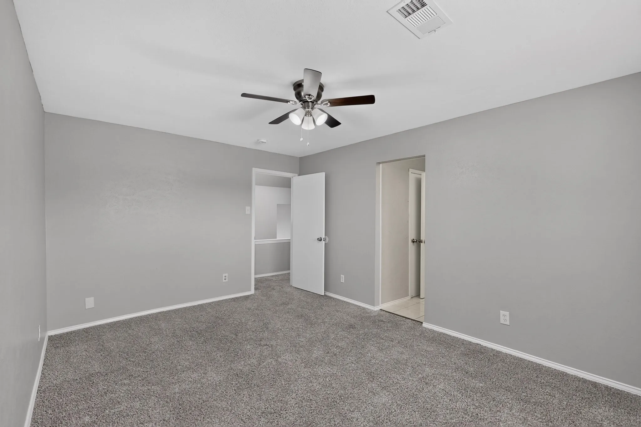 Neutral gray wall finish, gray carpet flooring, ceiling fan with light fixture, white trim, and white interior doors
