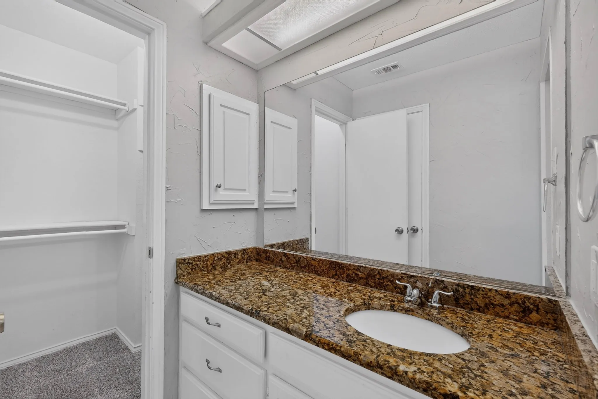 Vanity with a granite-style countertop, undermount sink, and chrome fixtures
