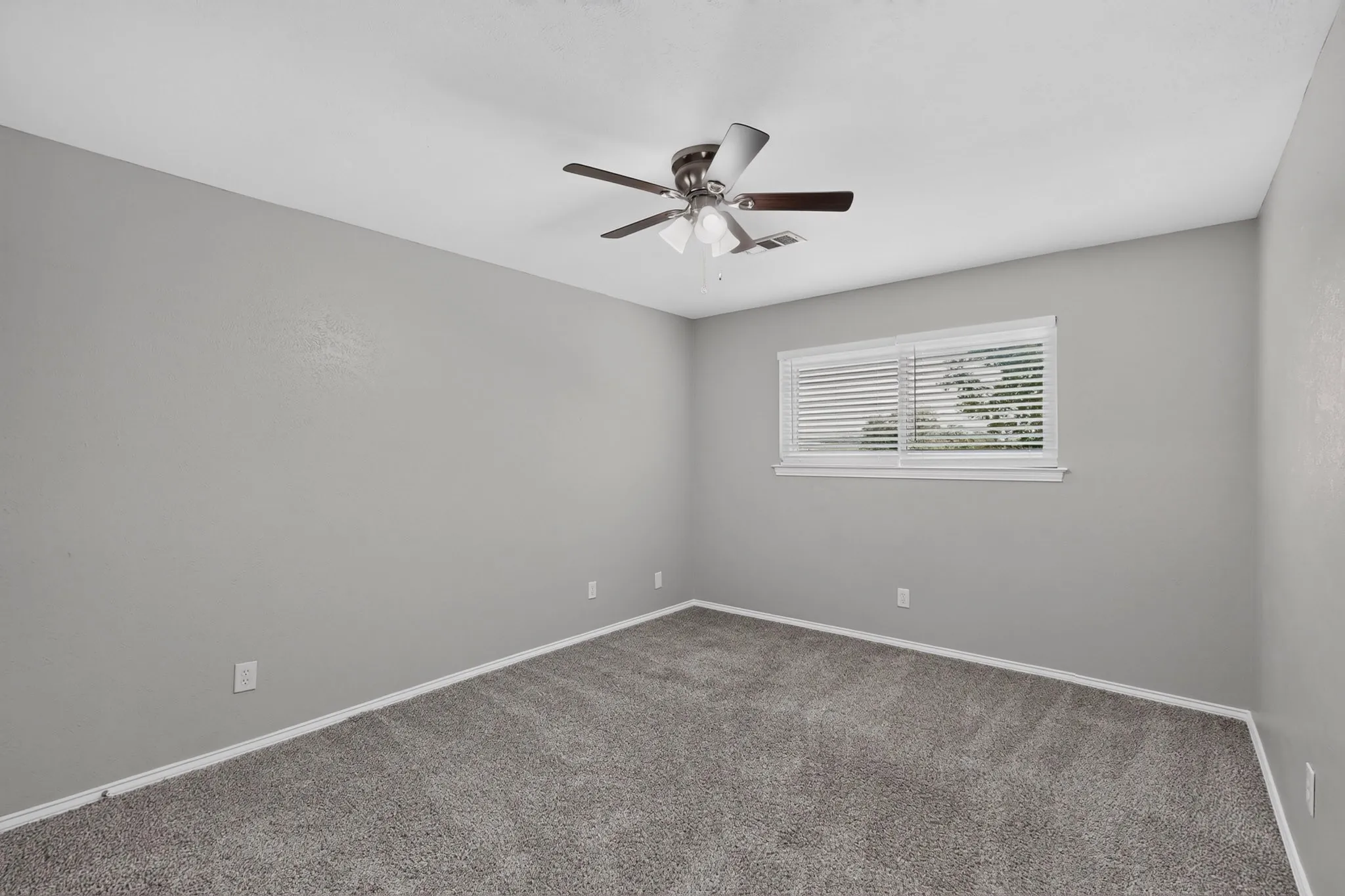 Gray carpeting and walls, a window with horizontal blinds, and a ceiling fan with integrated lighting