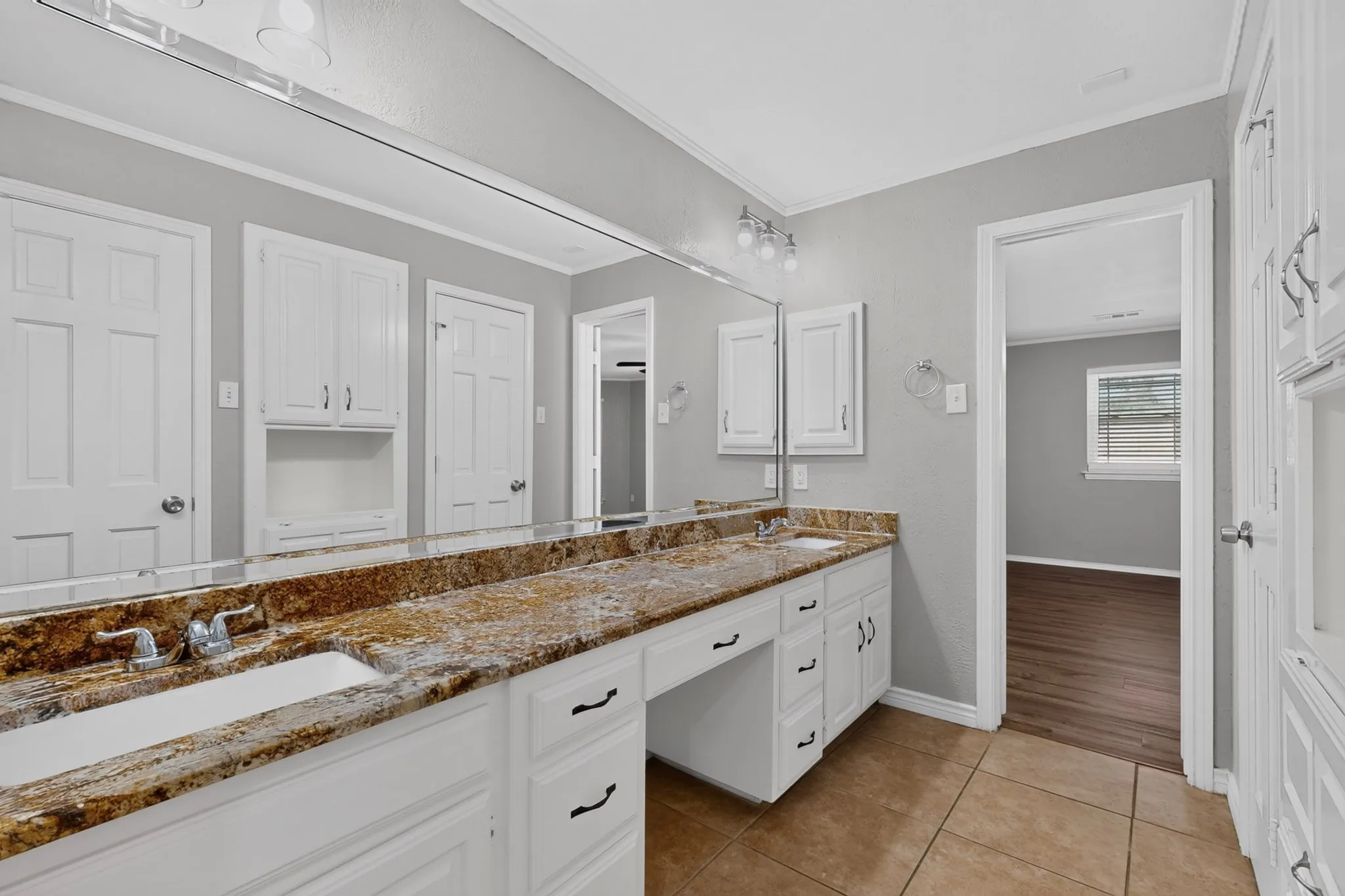 Dual sink vanity with stone-finish countertop, white cabinetry, and a full-width mirror