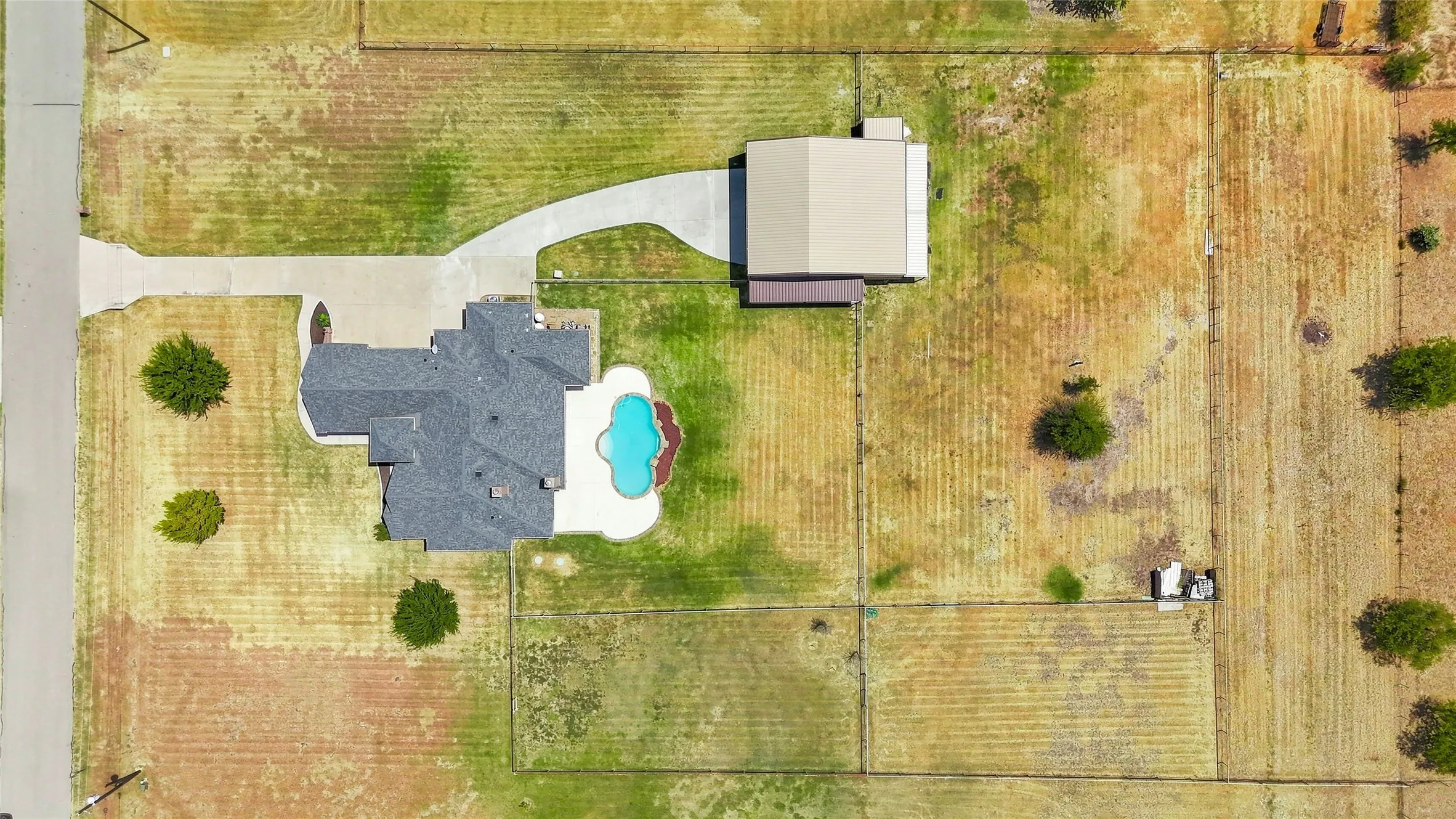 Paved driveway leading to a multi-level roofline residence with a swimming pool and a separate detached building