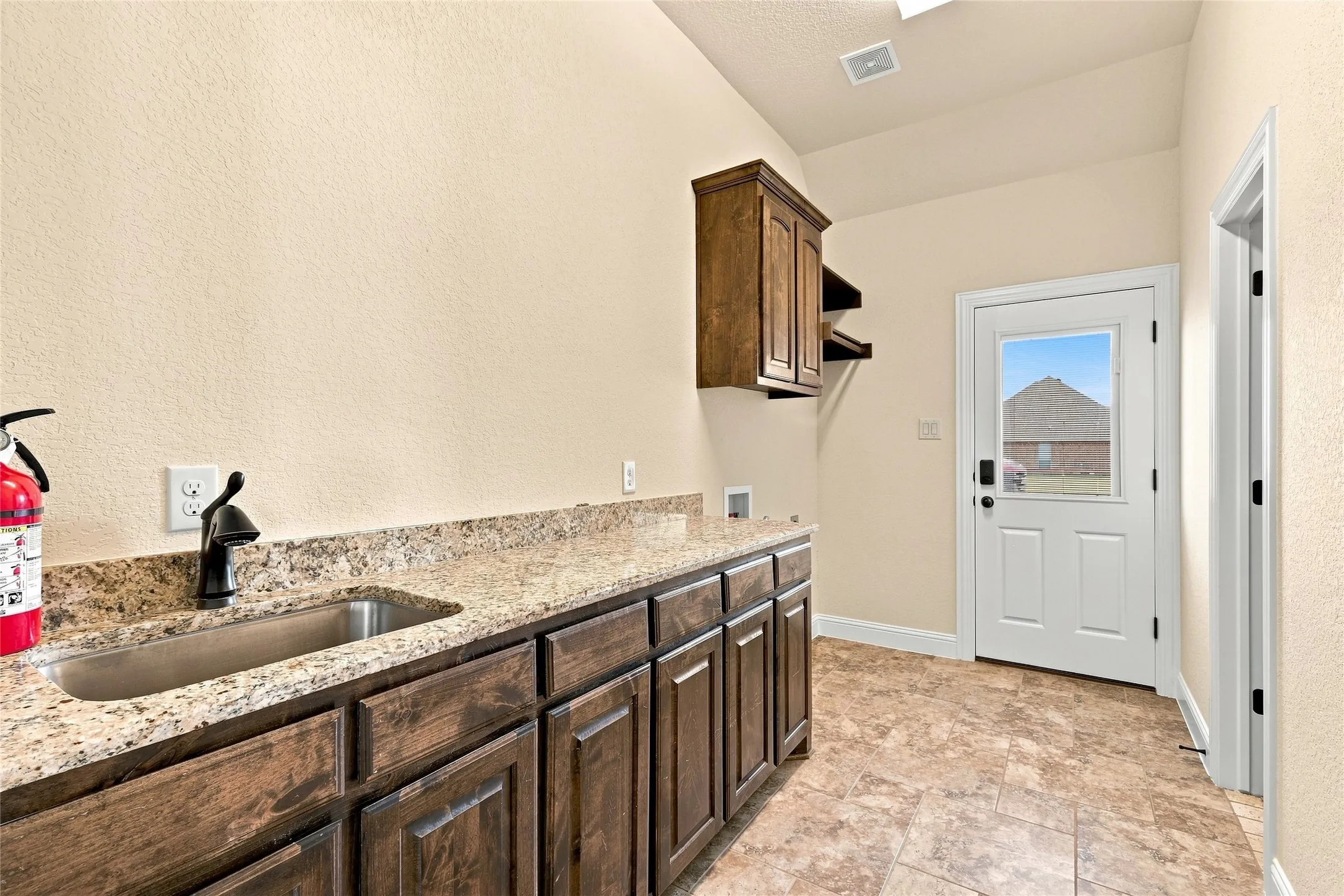 Built-in cabinetry with a granite-style countertop, stainless steel utility sink, and matte black faucet