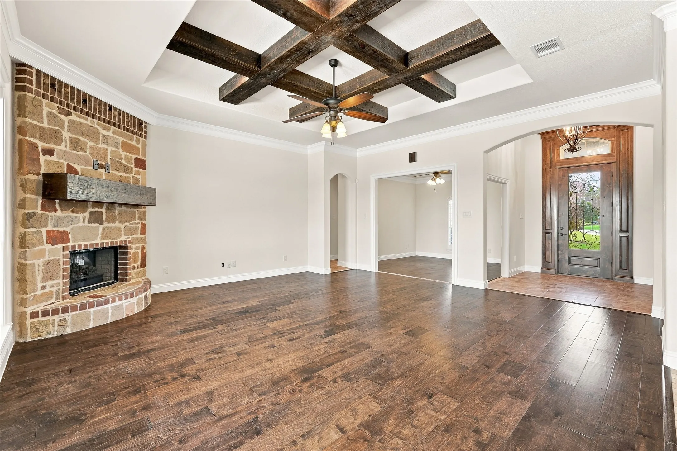 Spacious room featuring wood-finish flooring, a stone-clad fireplace with a wood mantel, and a tray ceiling with exposed wood beams