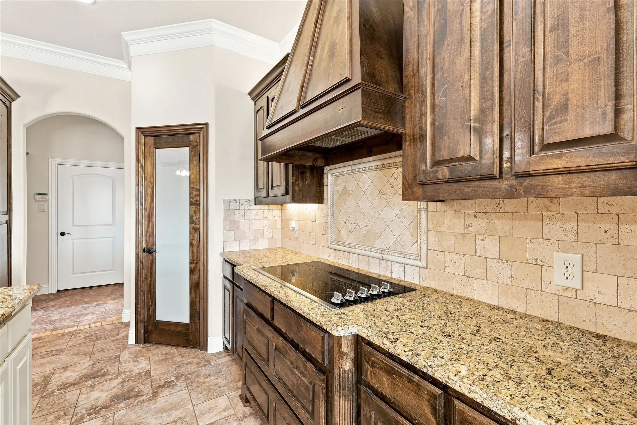 Built-in electric cooktop, granite countertops, wood-finish cabinetry, tile backsplash, and crown molding