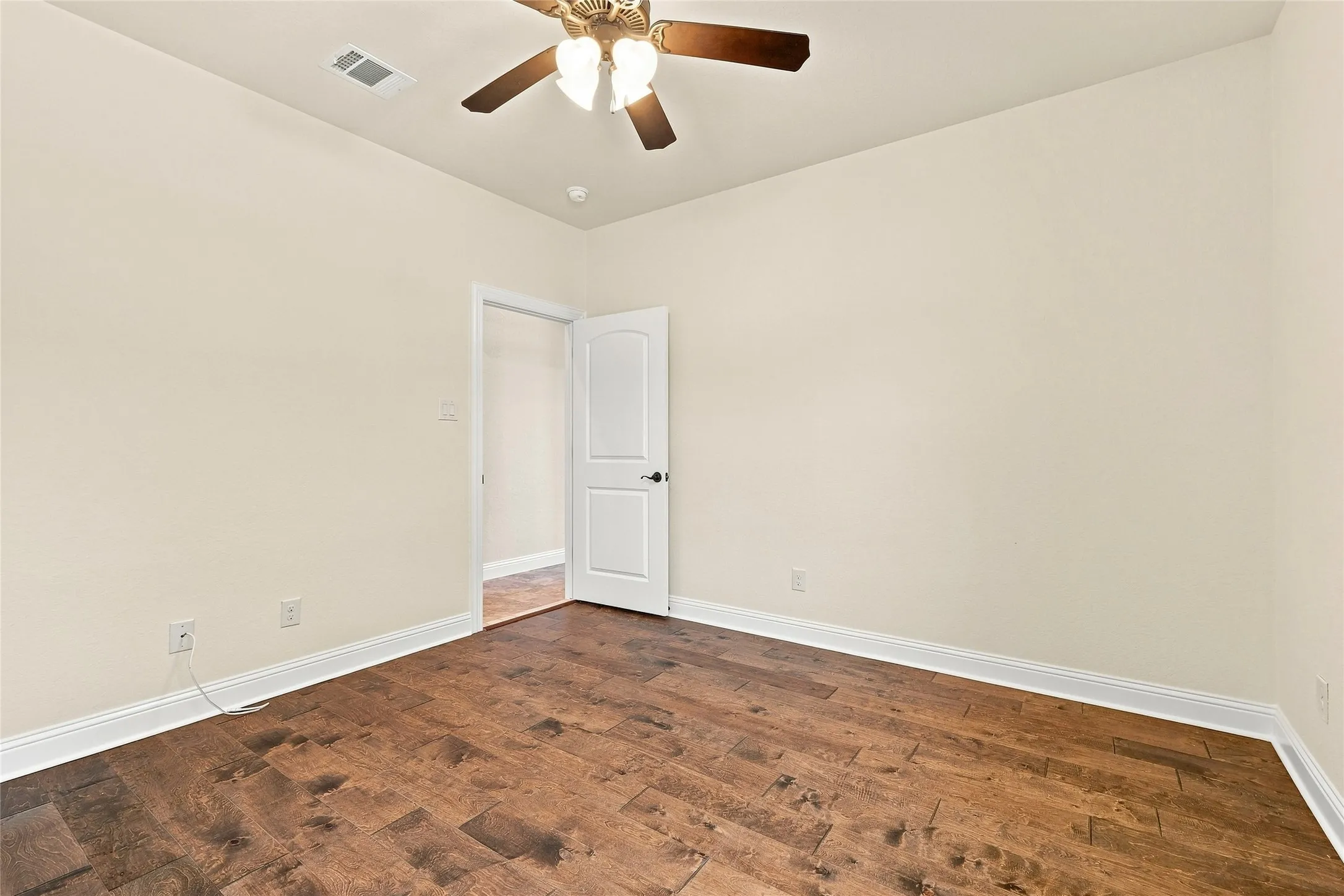 Wood-finish flooring, ceiling fan with integrated lighting, neutral wall palette, white trim, and a paneled interior door