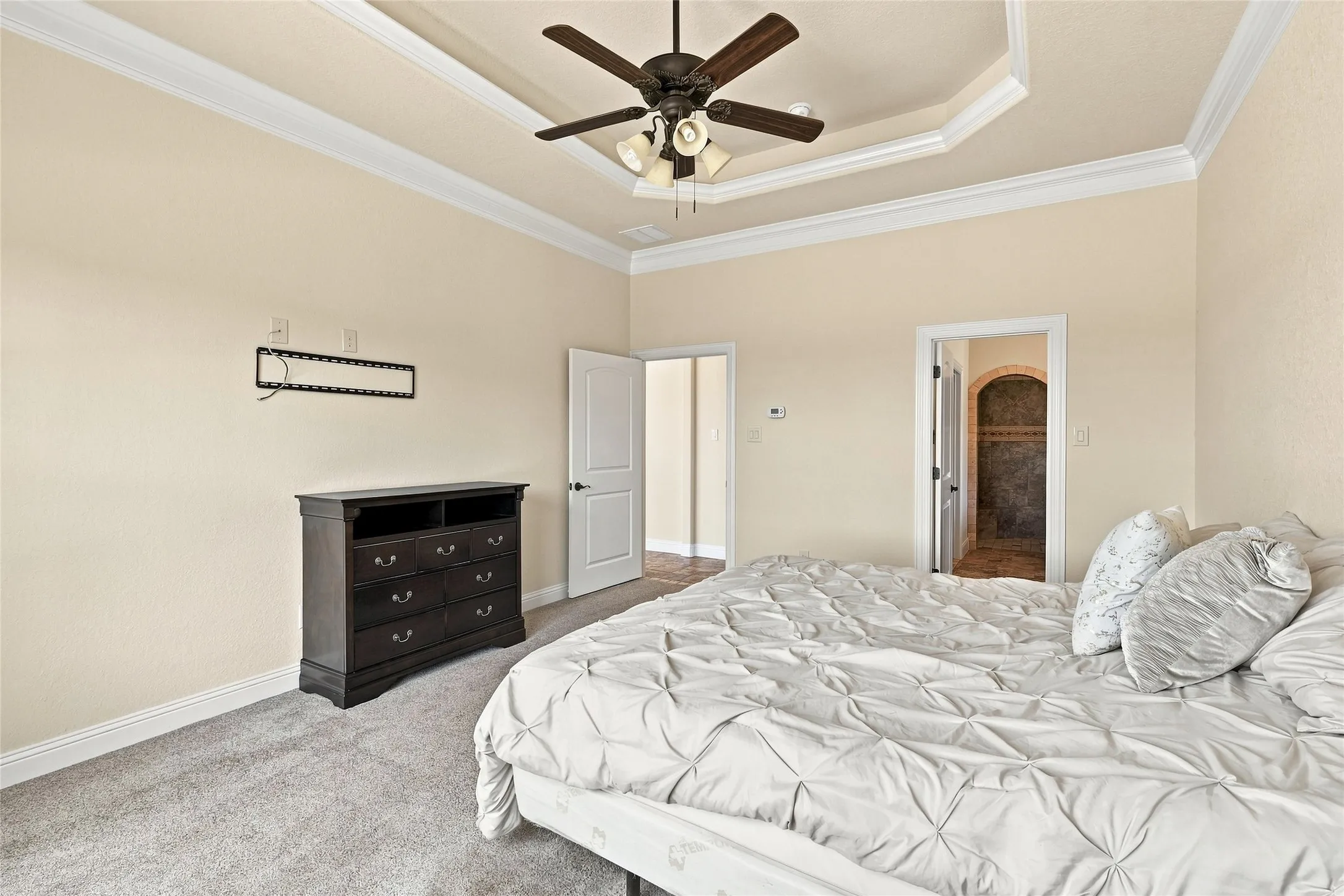 Tray ceiling with crown molding and a ceiling fan, light neutral wall paint, and gray carpet flooring