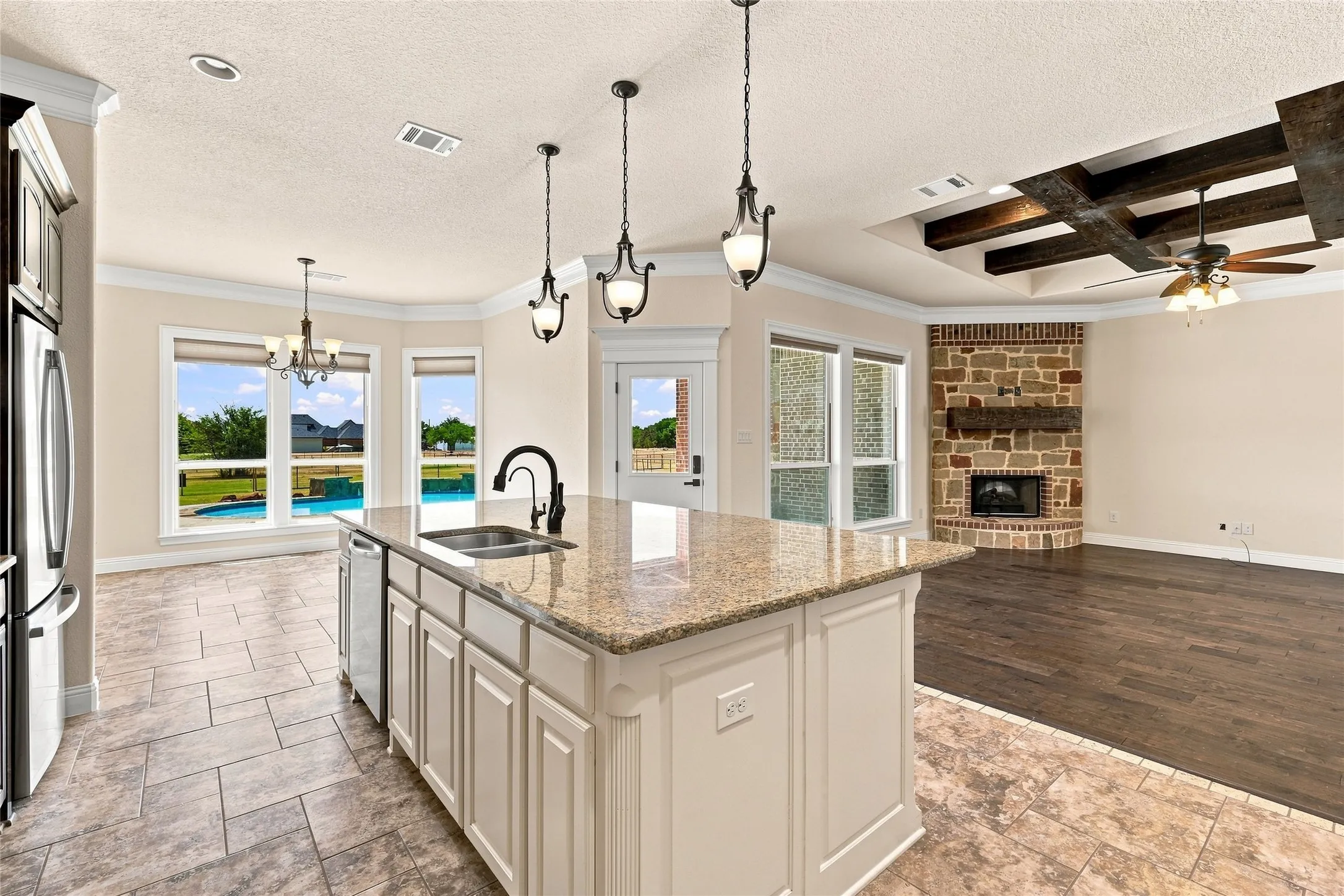 Kitchen island with granite countertop and integrated sink, stainless steel appliances, tile flooring, and custom ceiling with exposed beams