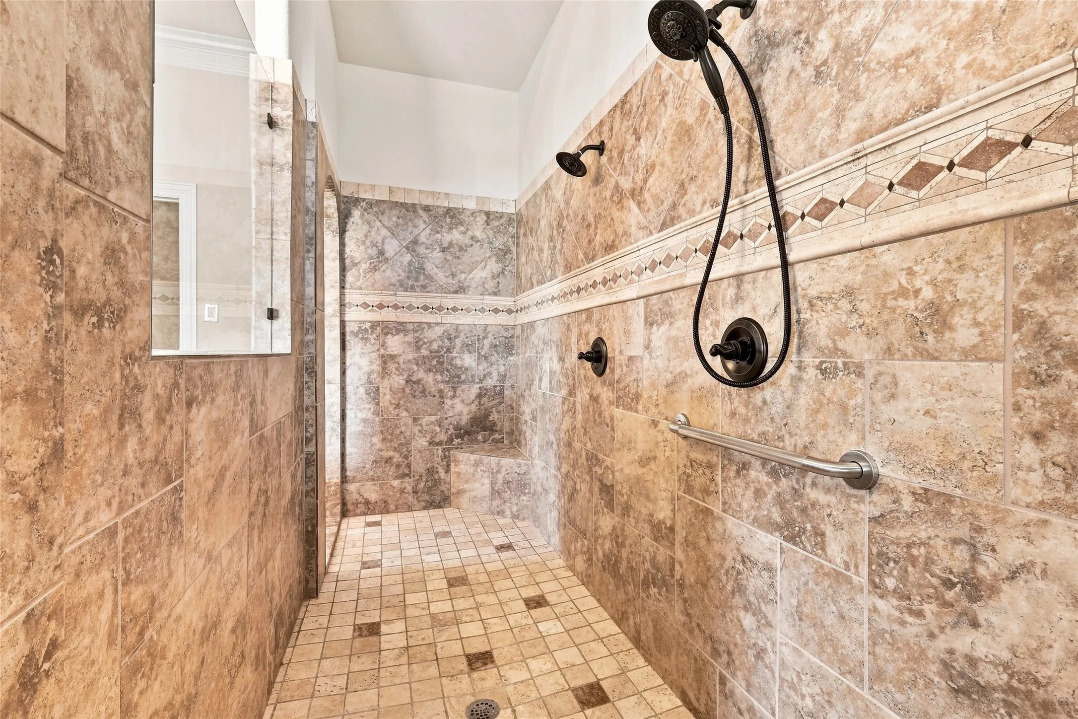 Walk-in shower with full wall tiling, patterned accent tile, built-in shower bench, and dark bronze fixtures