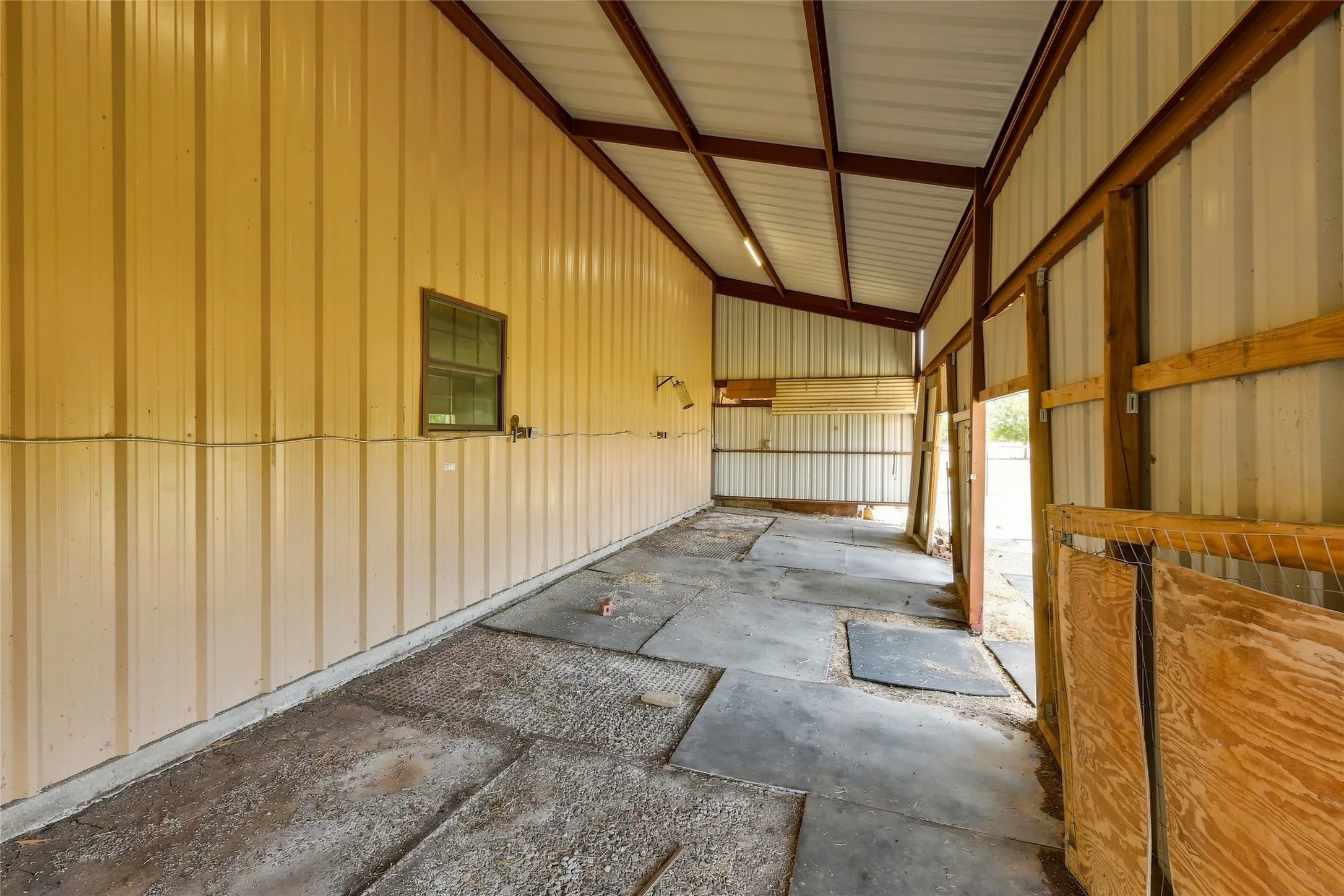 Metal-sided structure with exposed beam ceiling, concrete flooring, and a single window