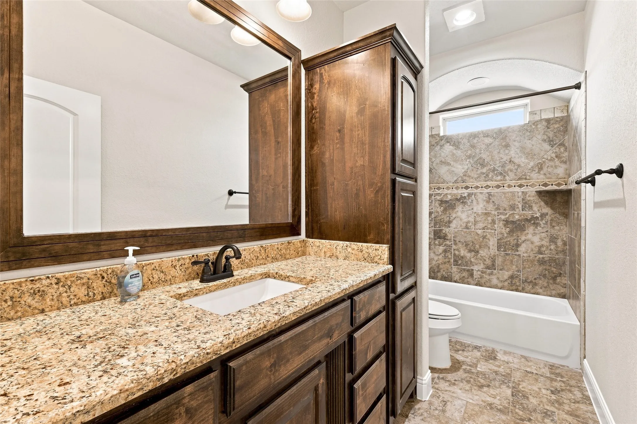 Granite-look countertop, wood-finish cabinetry, rectangular sink, bronze-finish faucet, and tiled shower surround