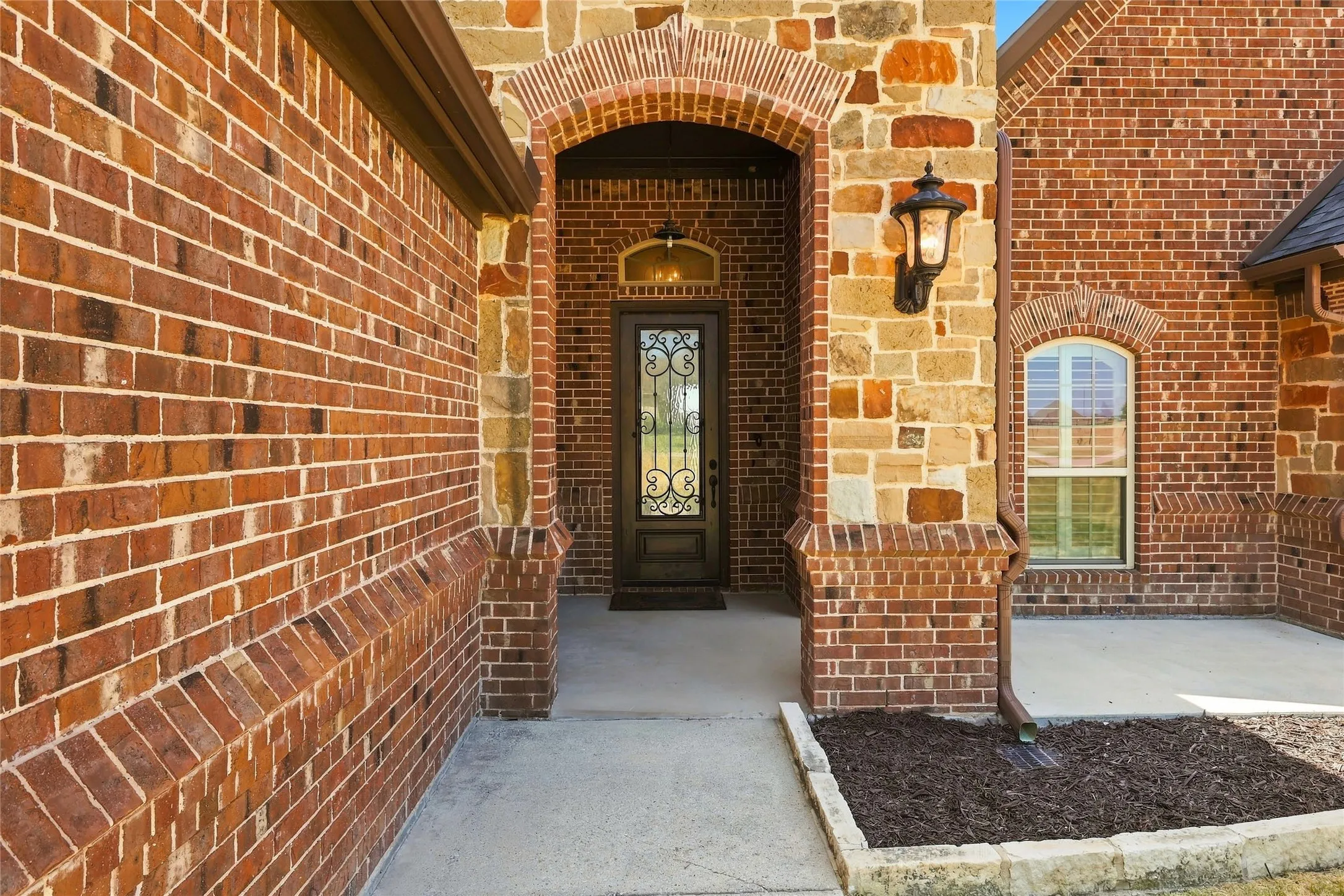 Brick and stone exterior featuring an arched entryway, decorative front door, and an exterior wall lantern