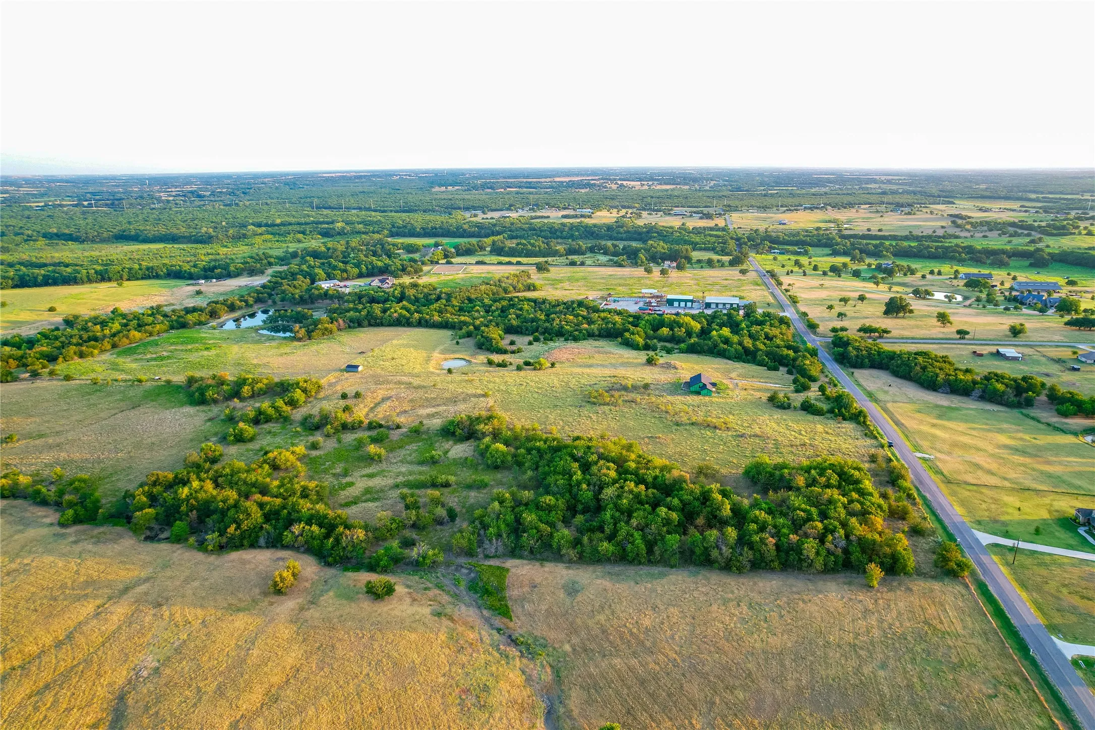 Expansive rural landscape featuring scattered trees, open fields, and multiple ponds