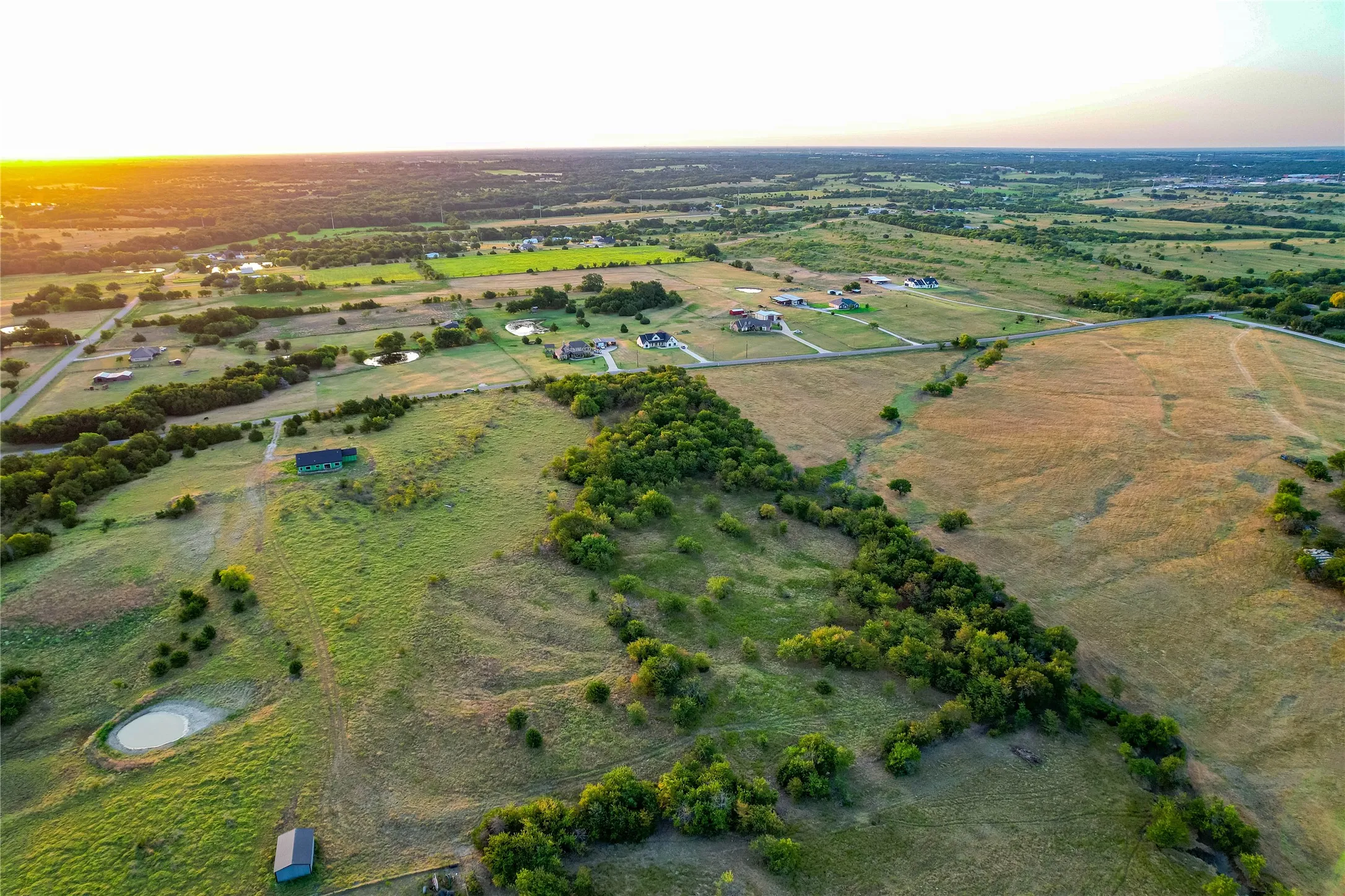 Expansive rural landscape featuring scattered residential properties, mature tree lines, and open grasslands