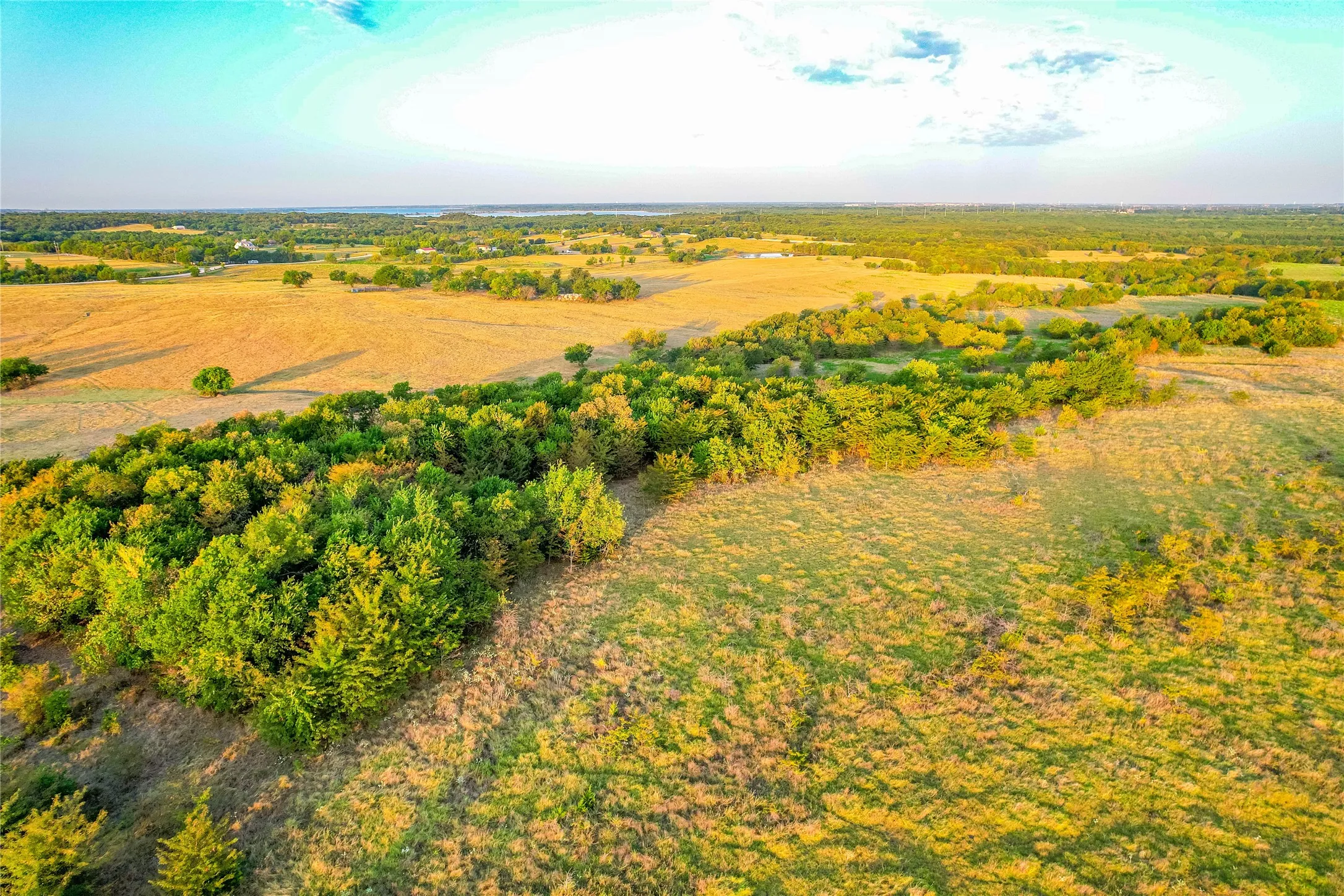 Expansive land featuring a mix of open fields and mature tree lines