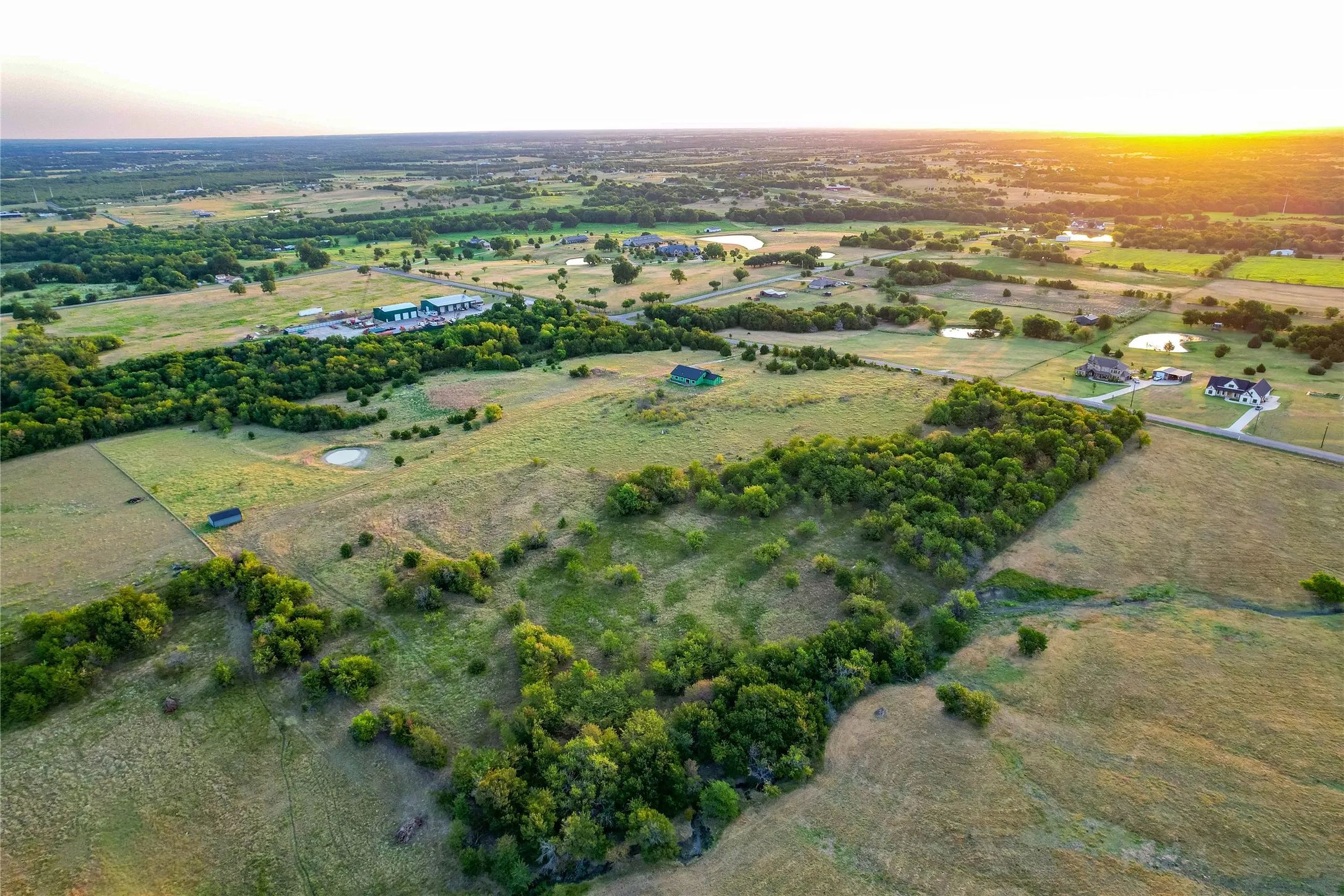 Expansive rural landscape with scattered trees, a visible pond, and multiple residential structures