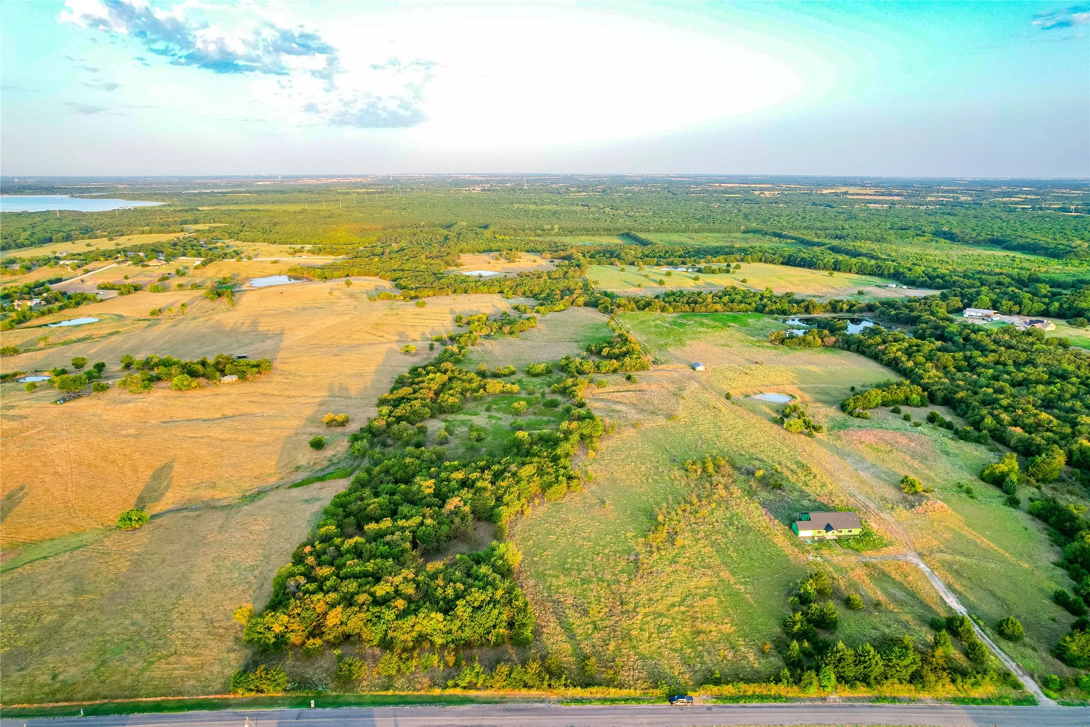 Expansive acreage featuring a body of water, scattered trees, and a distant residence
