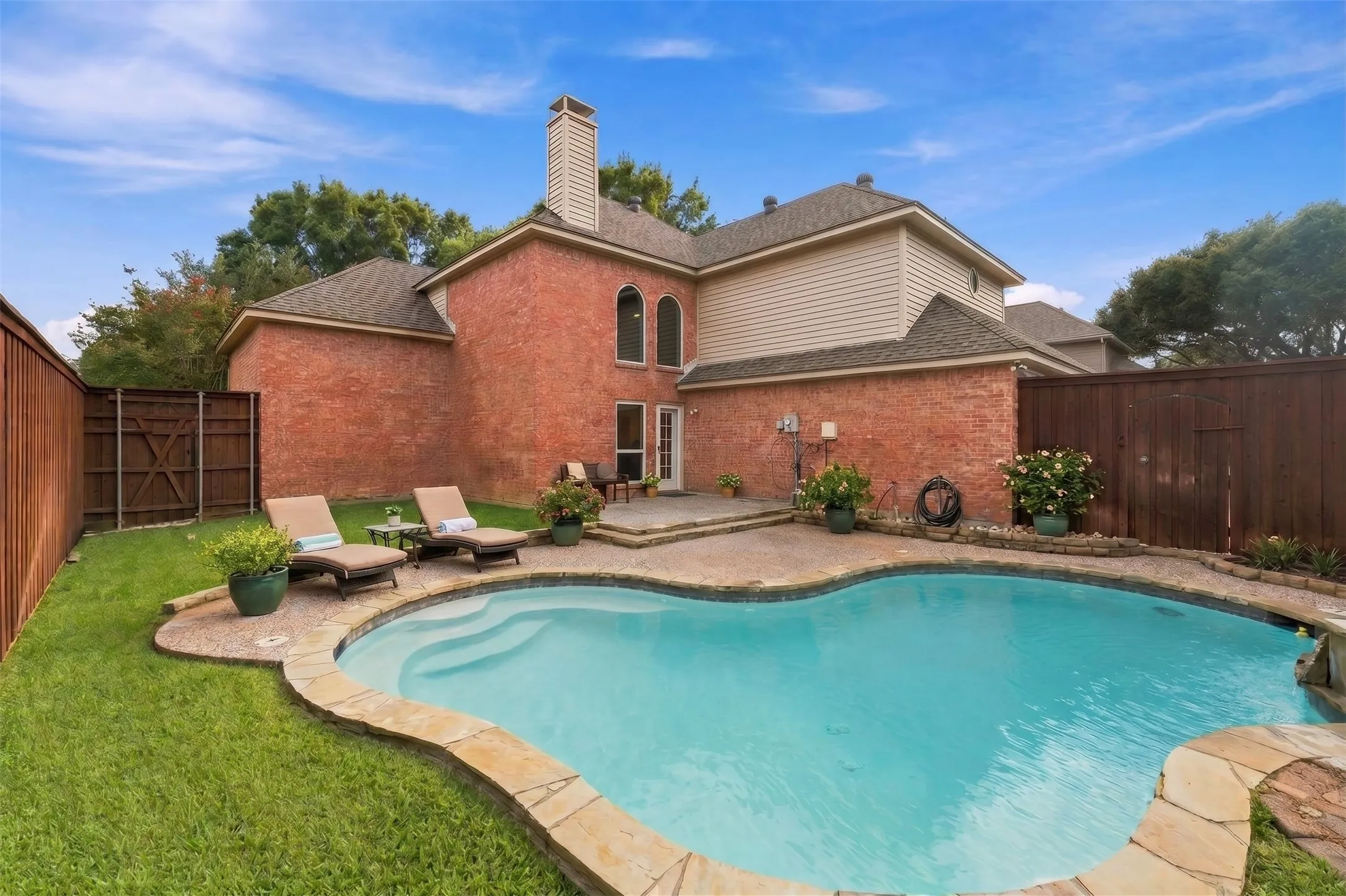 AI generated outdoor furniture and accessories. Brick exterior with siding accents, freeform swimming pool, stone coping, patio with brick pavers, and a wood privacy fence