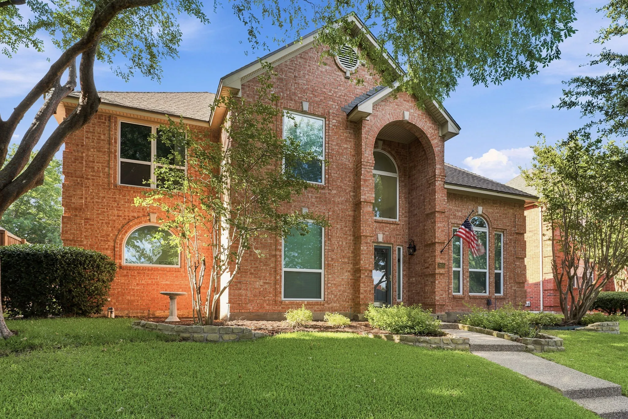 Brick exterior with arched entry, varied window styles, established landscaping, and a concrete walkway